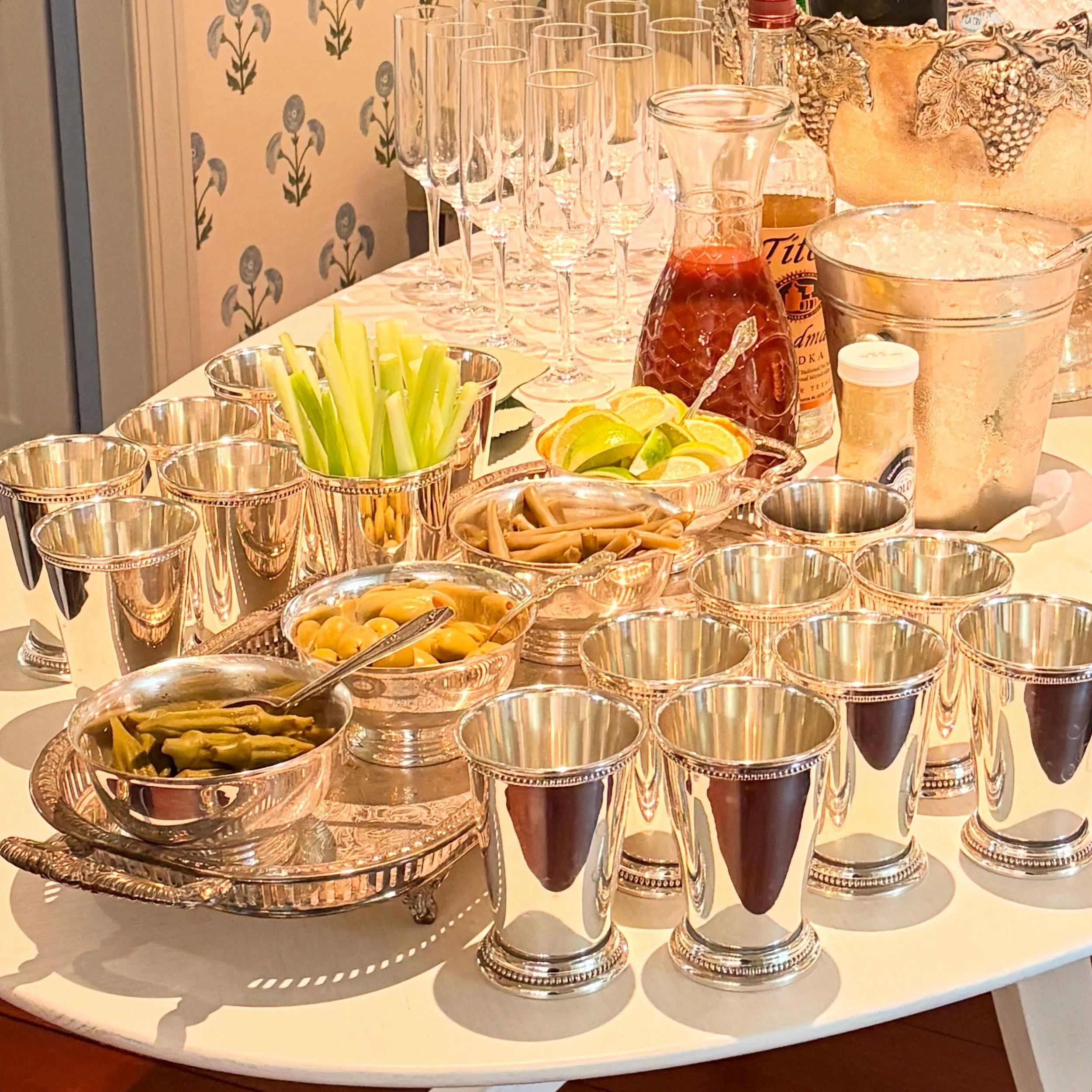 A Bloody Mary bar with silver revere bowls of pickled okra, green beans and olives alongside lemons, limes, celery and horseradish.  Cheers!