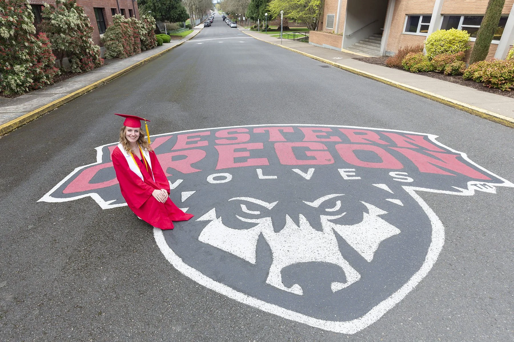 College graduate posing by the iconic Western Oregon Wolves sign on campus