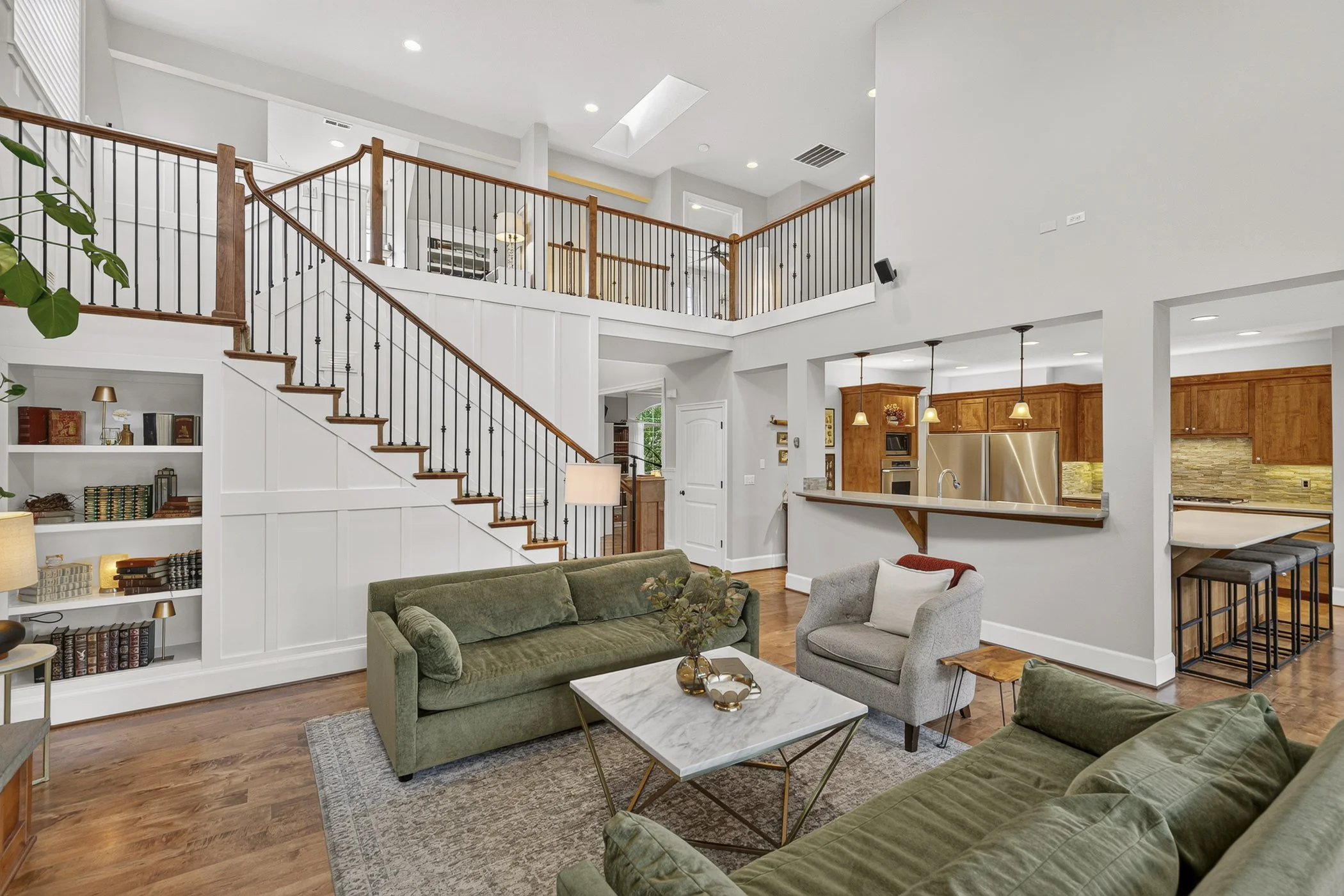 Open concept floor plan view of a living room space with a long staircase and kitchen in the background