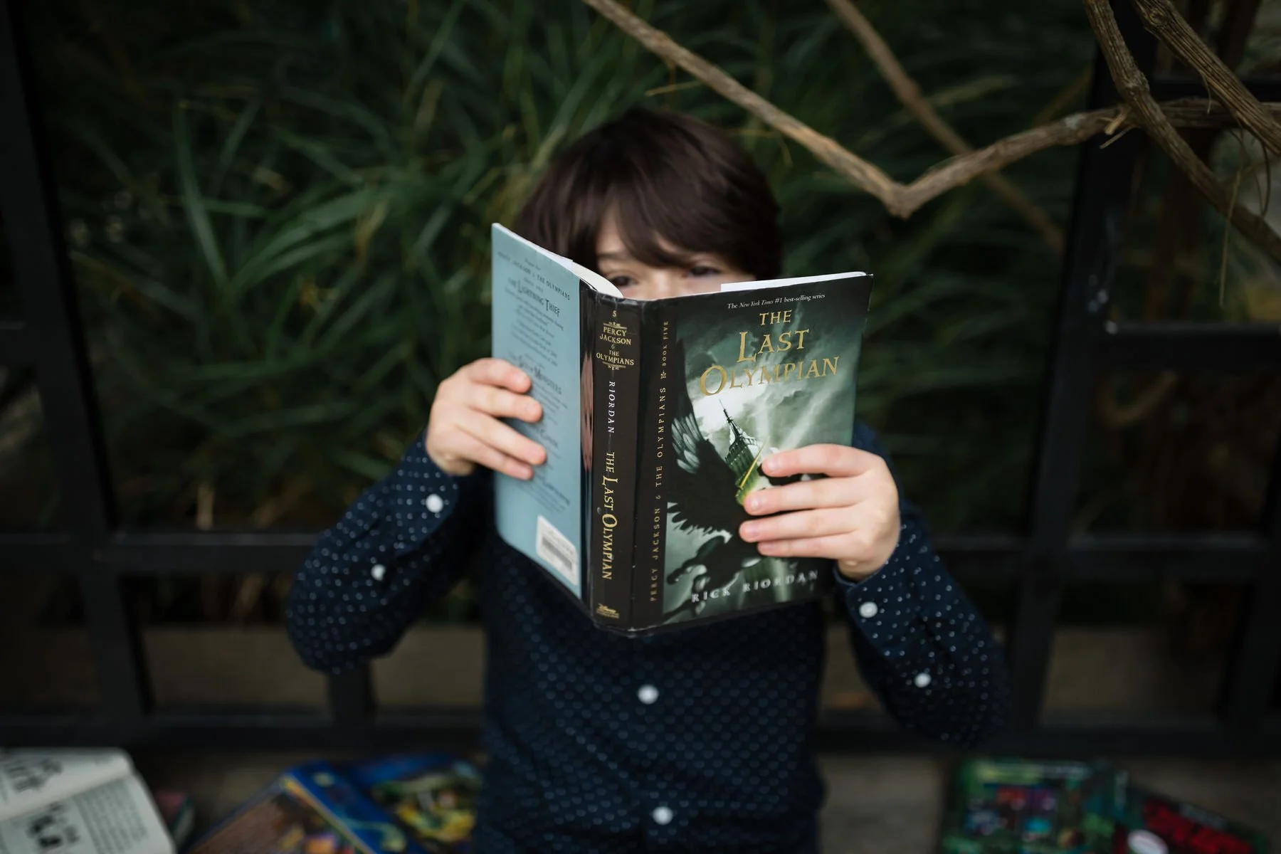 boy holds book last olympian in front of face