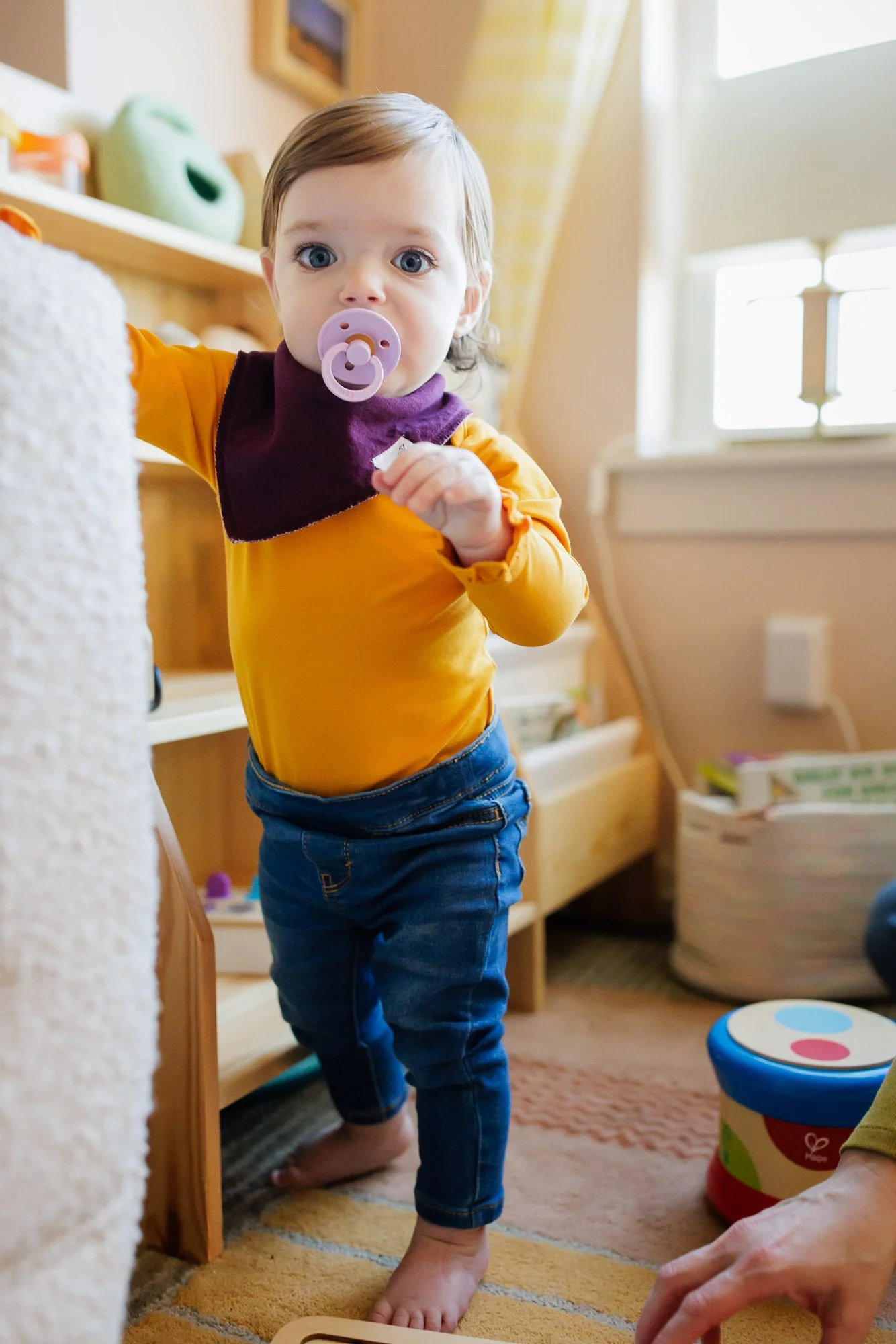 toddler with purple pacifier explores living room and toys