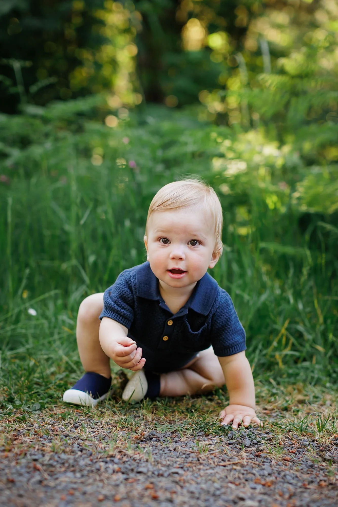 one year old boy in blue crawling in a park looking at the photograhper