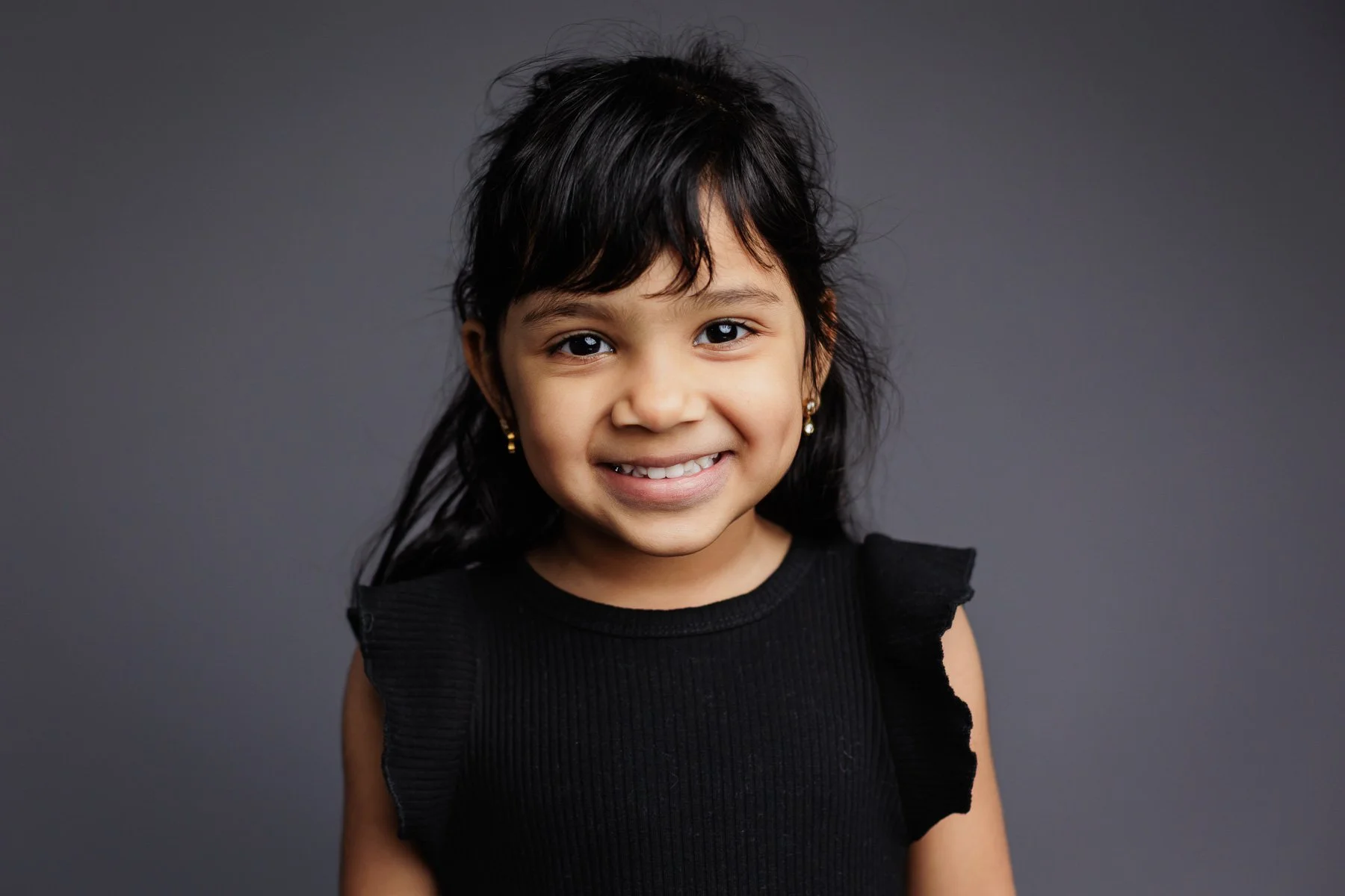 preschooler with dark hair and black dress smiling for school photo