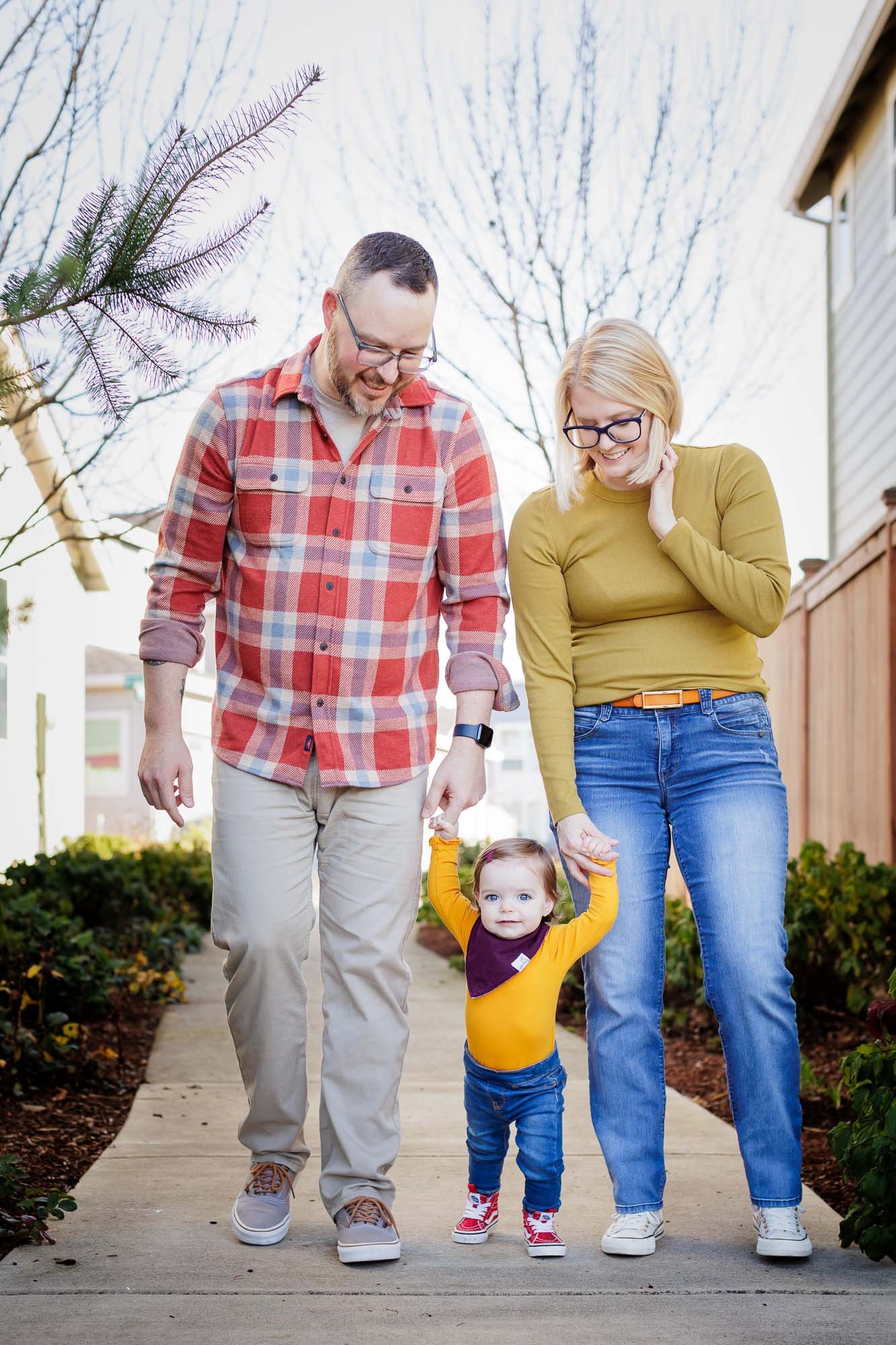 parents walk outside home holding toddlers hands who is learning to walk