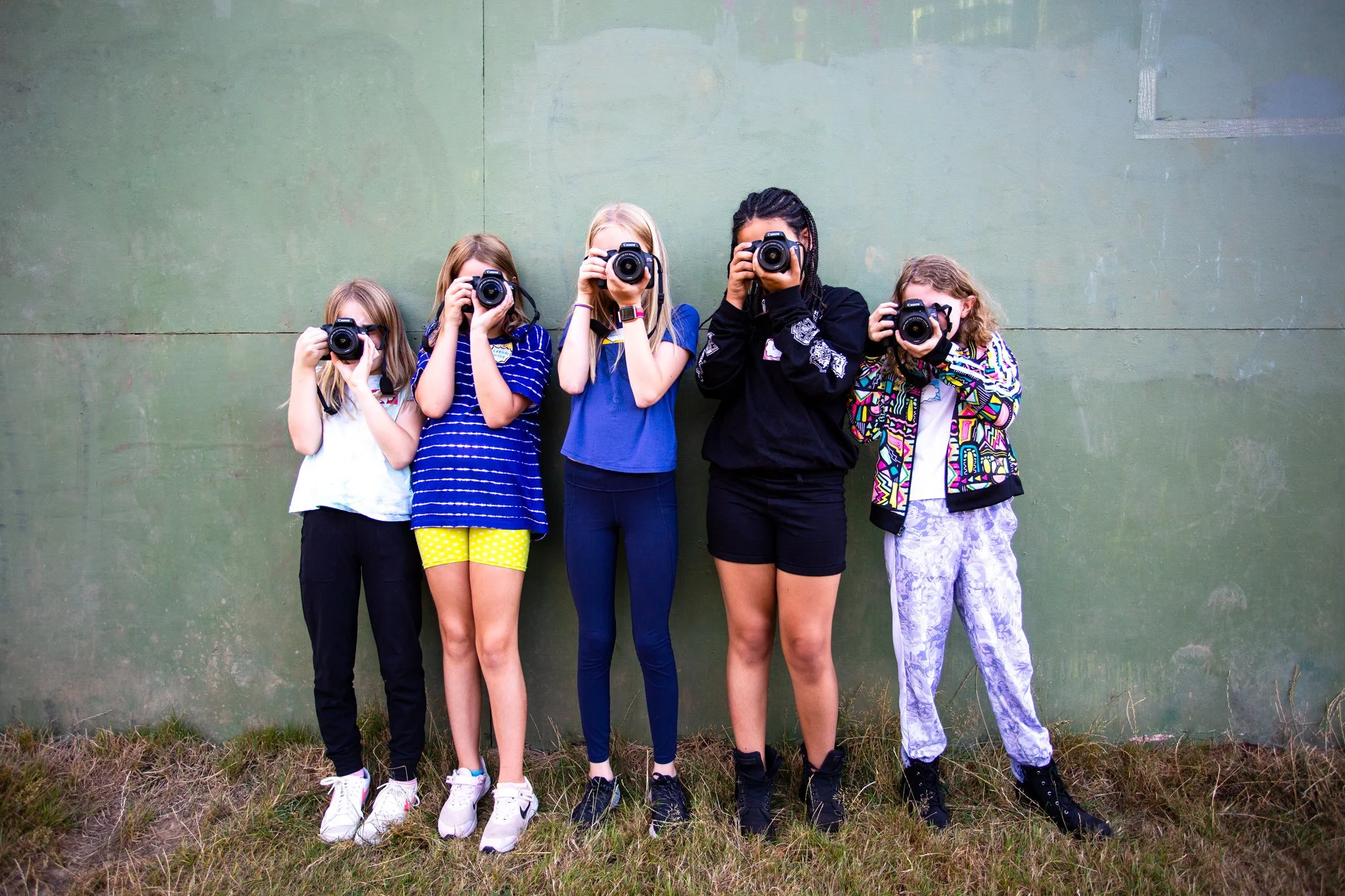 five kids holding cameras in front of green wall