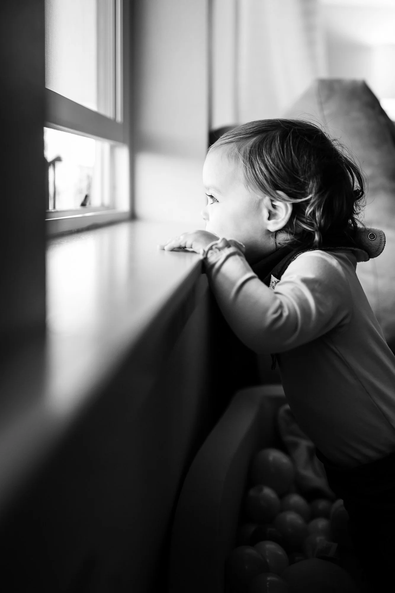 black and white image of toddler looking out a window