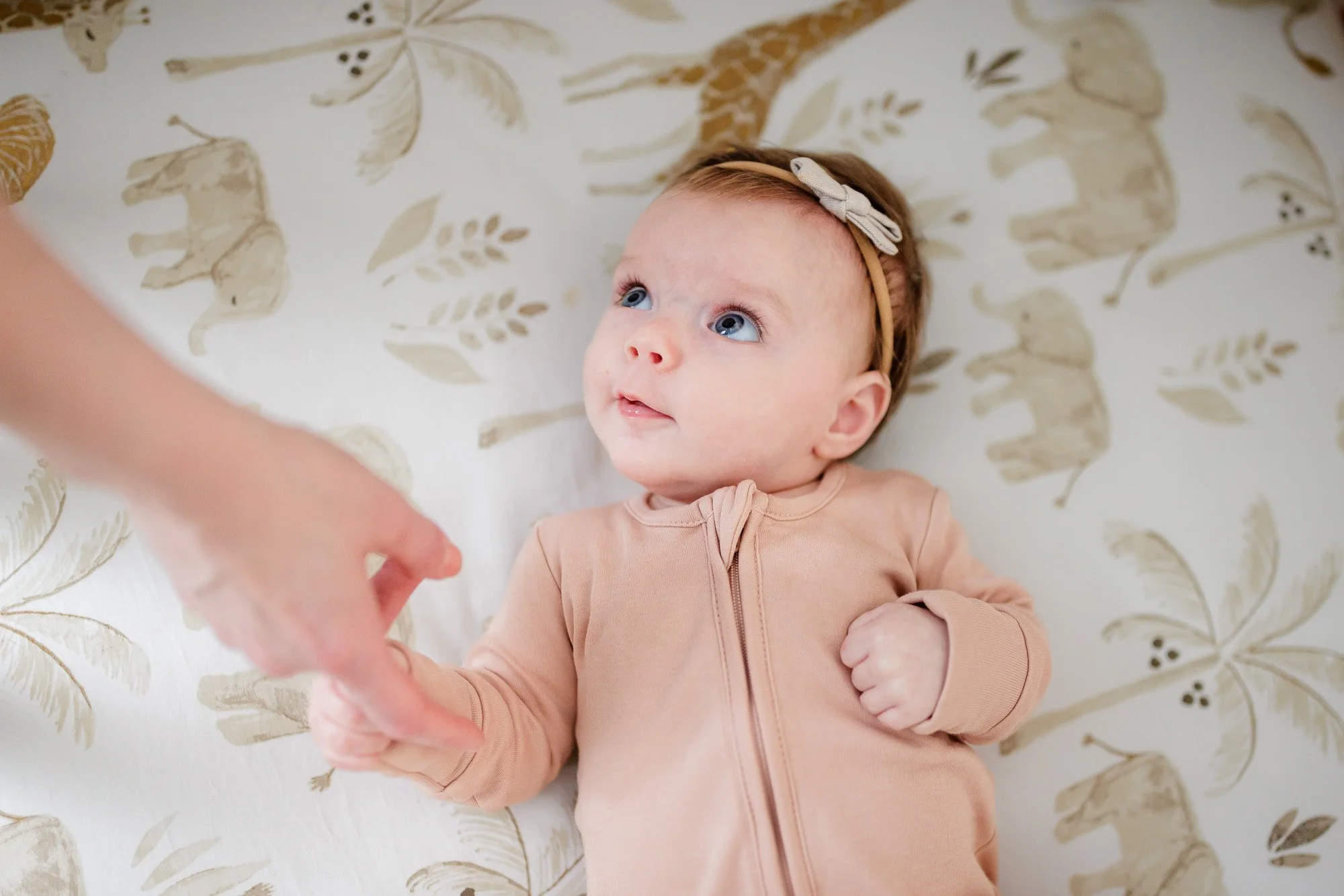 newborn baby looks up at parents from crib while holding hand