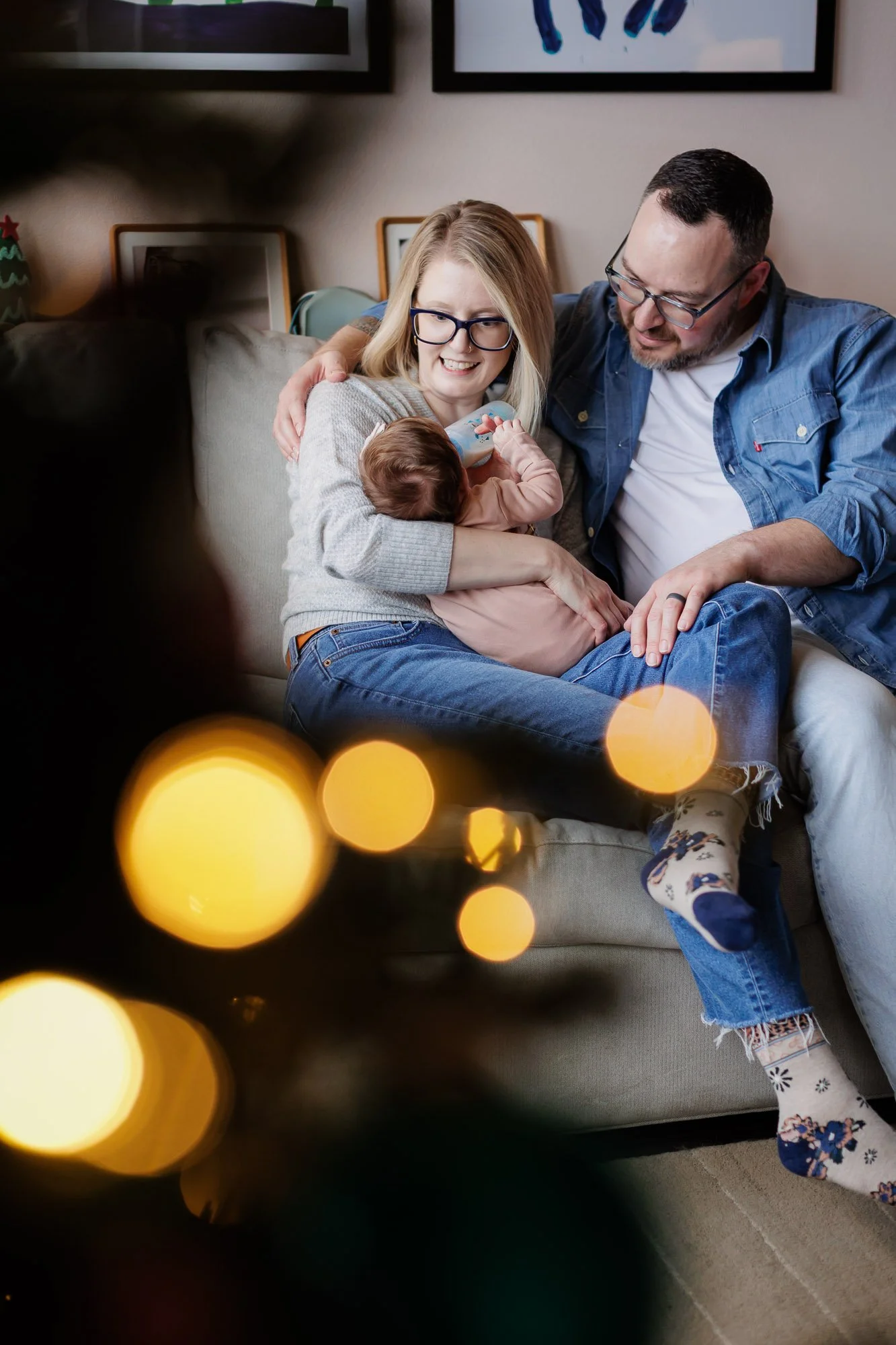 parents hold baby feeding bottle as viewed through Christmas tree