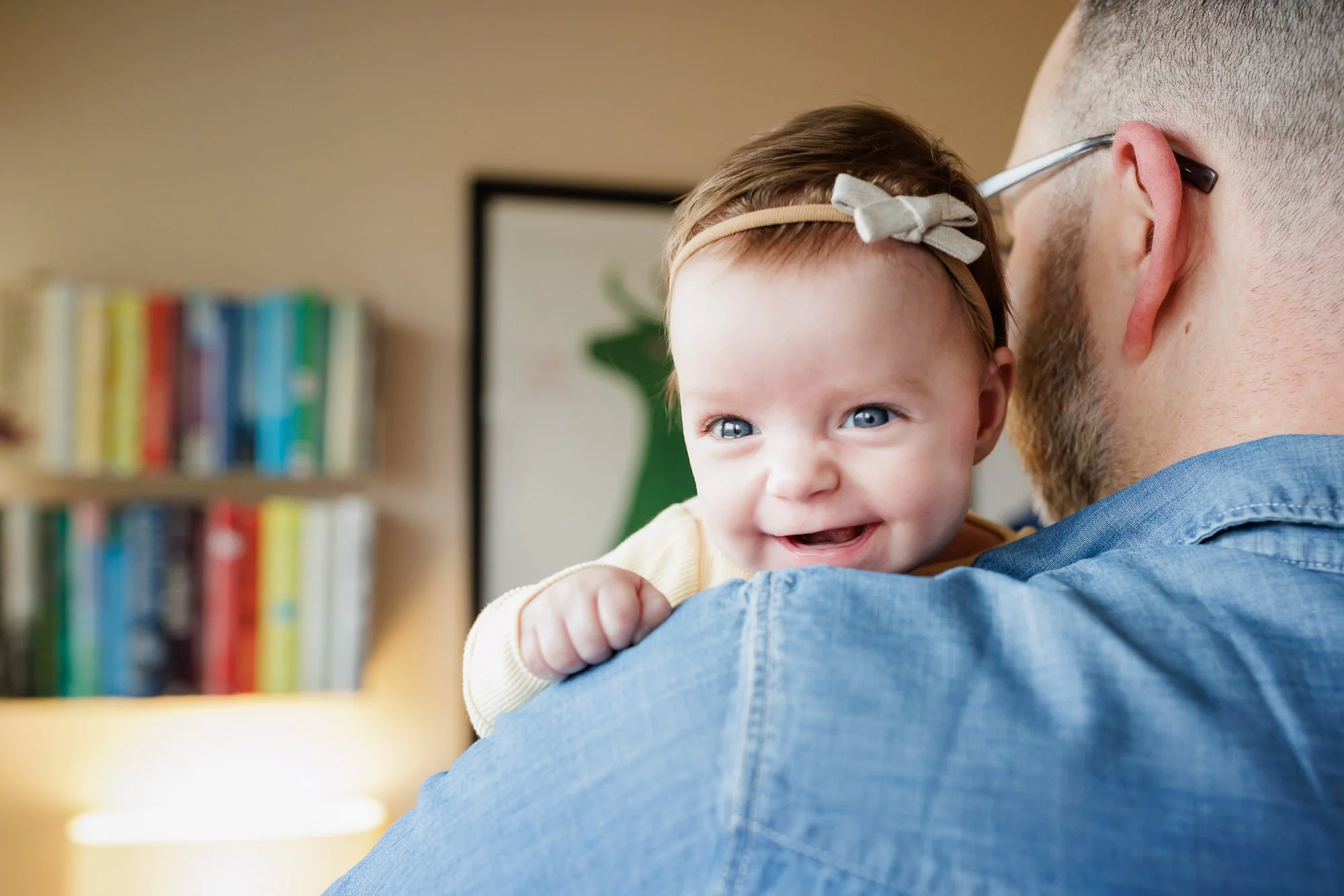 newborn with bow looks over dads shoulder while smiling
