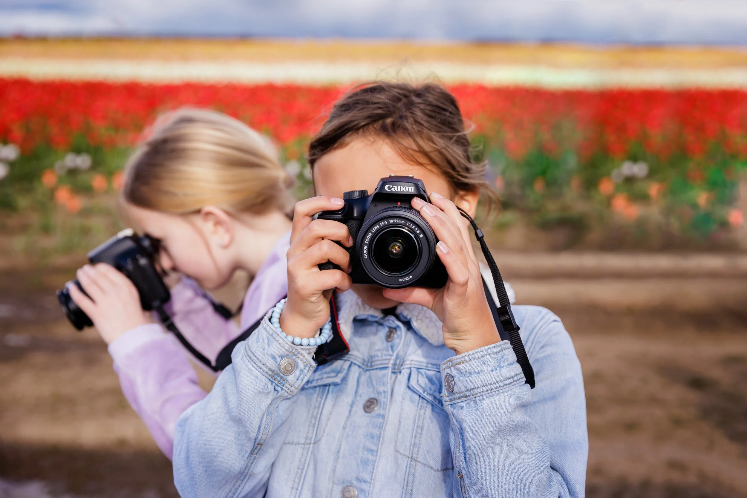 girl in jean jacket holds camera while in tulip field