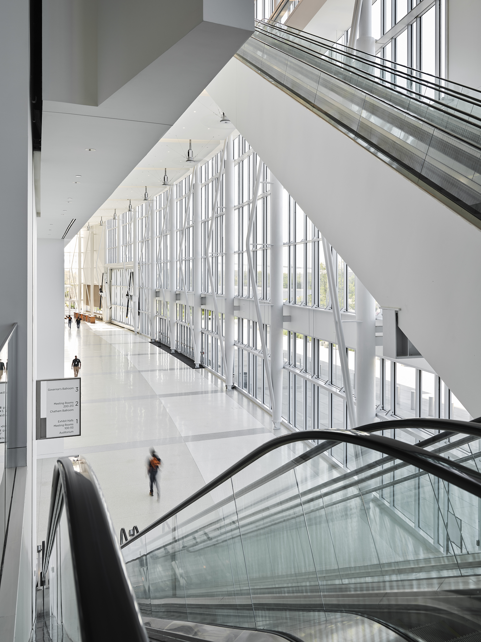 A wide-angle interior architectural photograph of the Savannah Convention Center expansion at twilight, showing the elevators leading to the first floor
