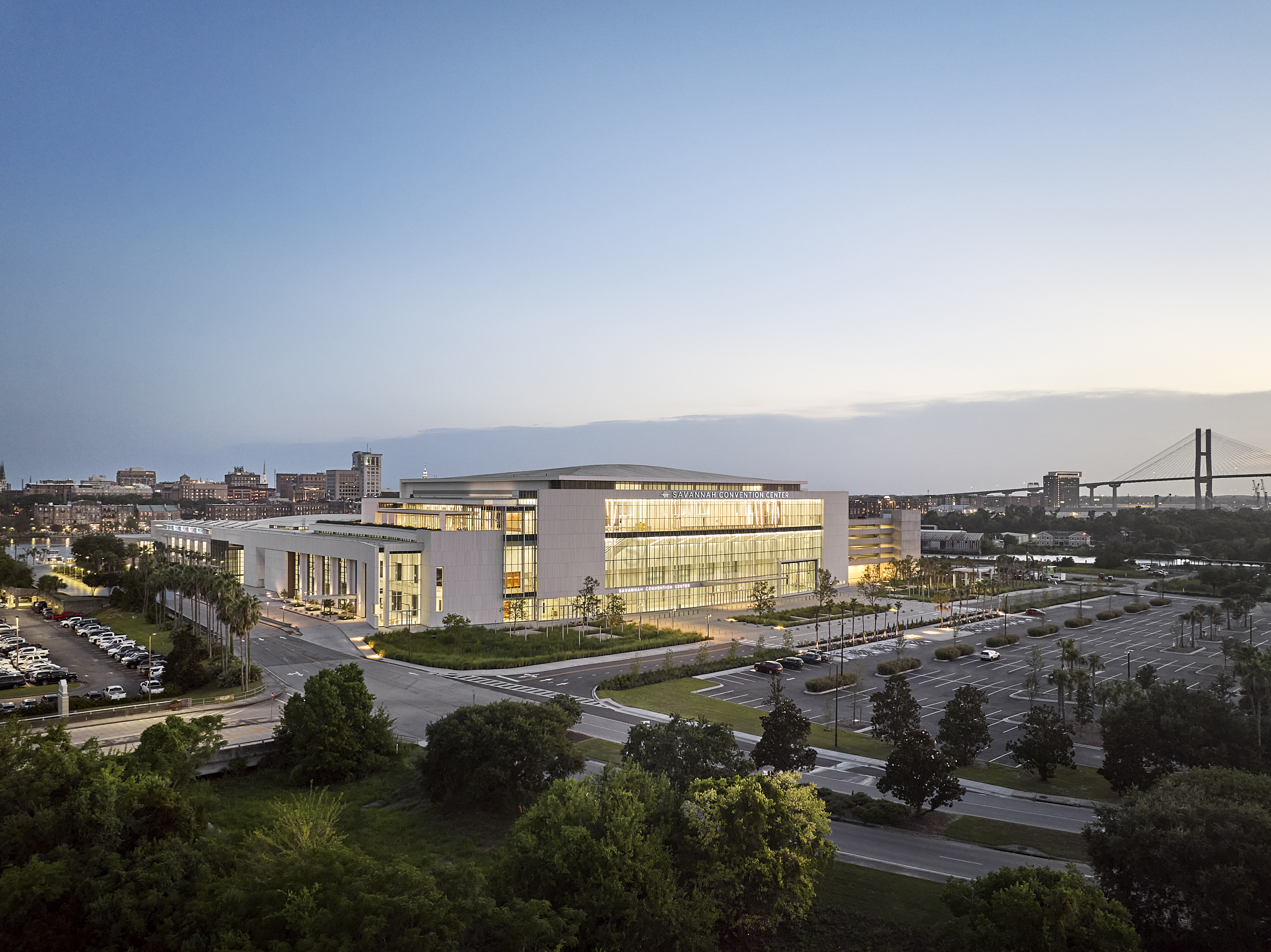 A wide-angle exterior architectural photograph of the Savannah Convention Center expansion at blue hour, showing the glass facade and parking lot

