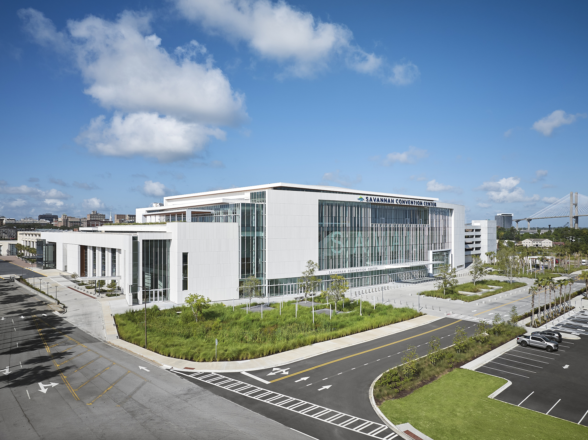 A wide-angle exterior architectural photograph of the Savannah Convention Center expansion with blue sky, showing the glass facade and clean lines of the building