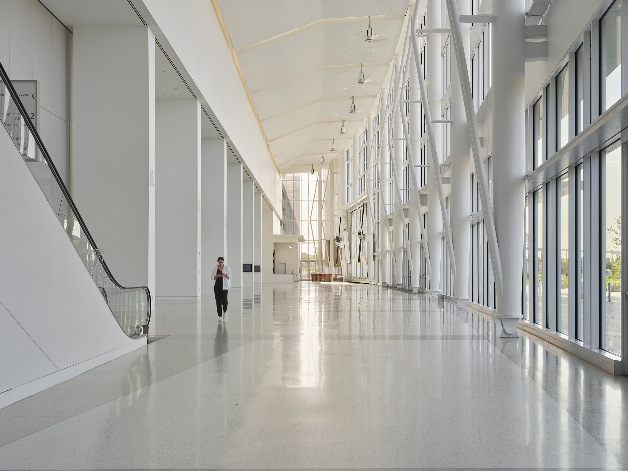A wide-angle interior architectural photograph of the Savannah Convention Center expansion at golden hour, showing the glass facade and main entrance