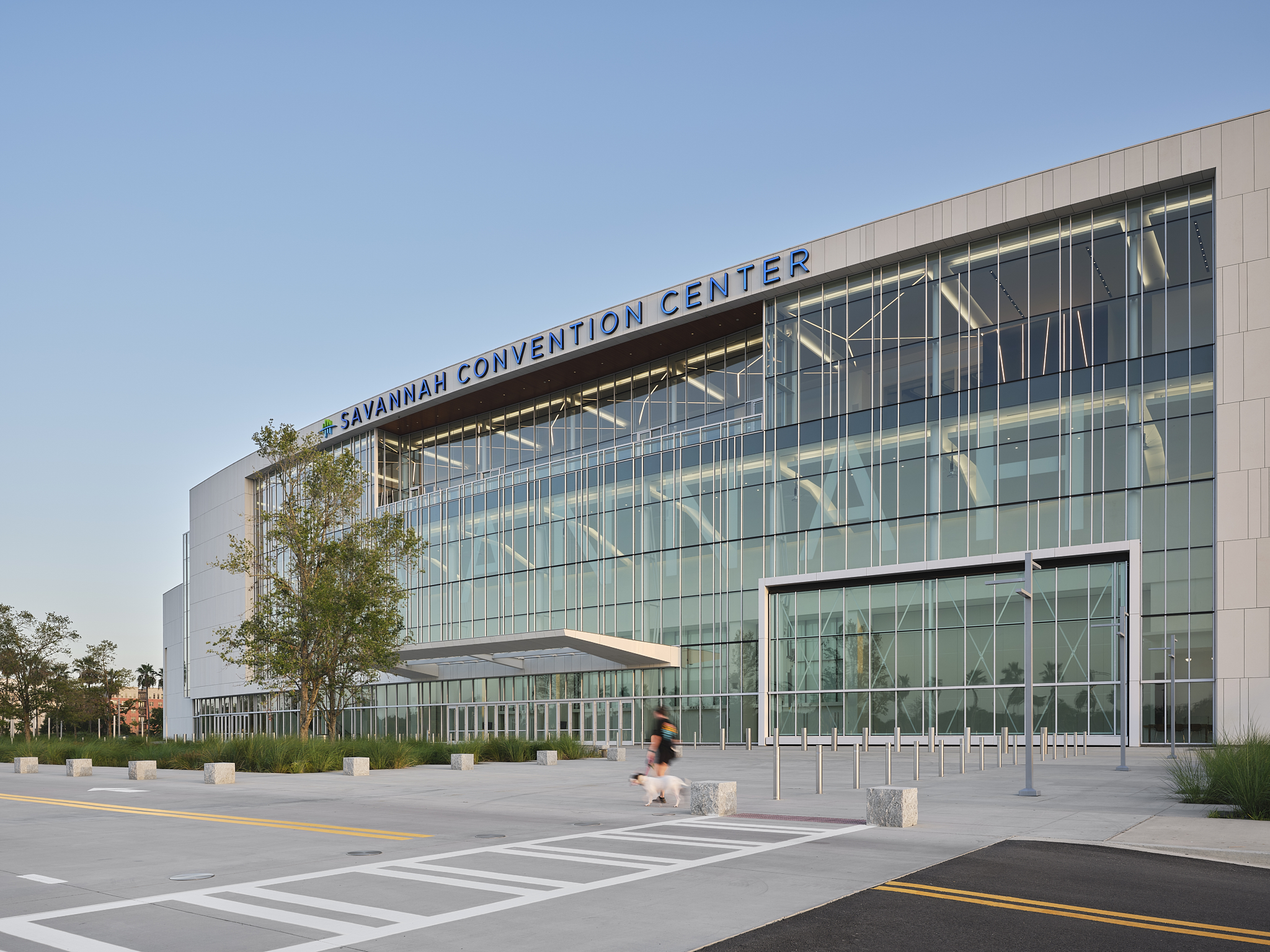 A wide-angle exterior architectural photograph of the Savannah Convention Center expansion during the afternoon, showing the glass facade and hangar doors
