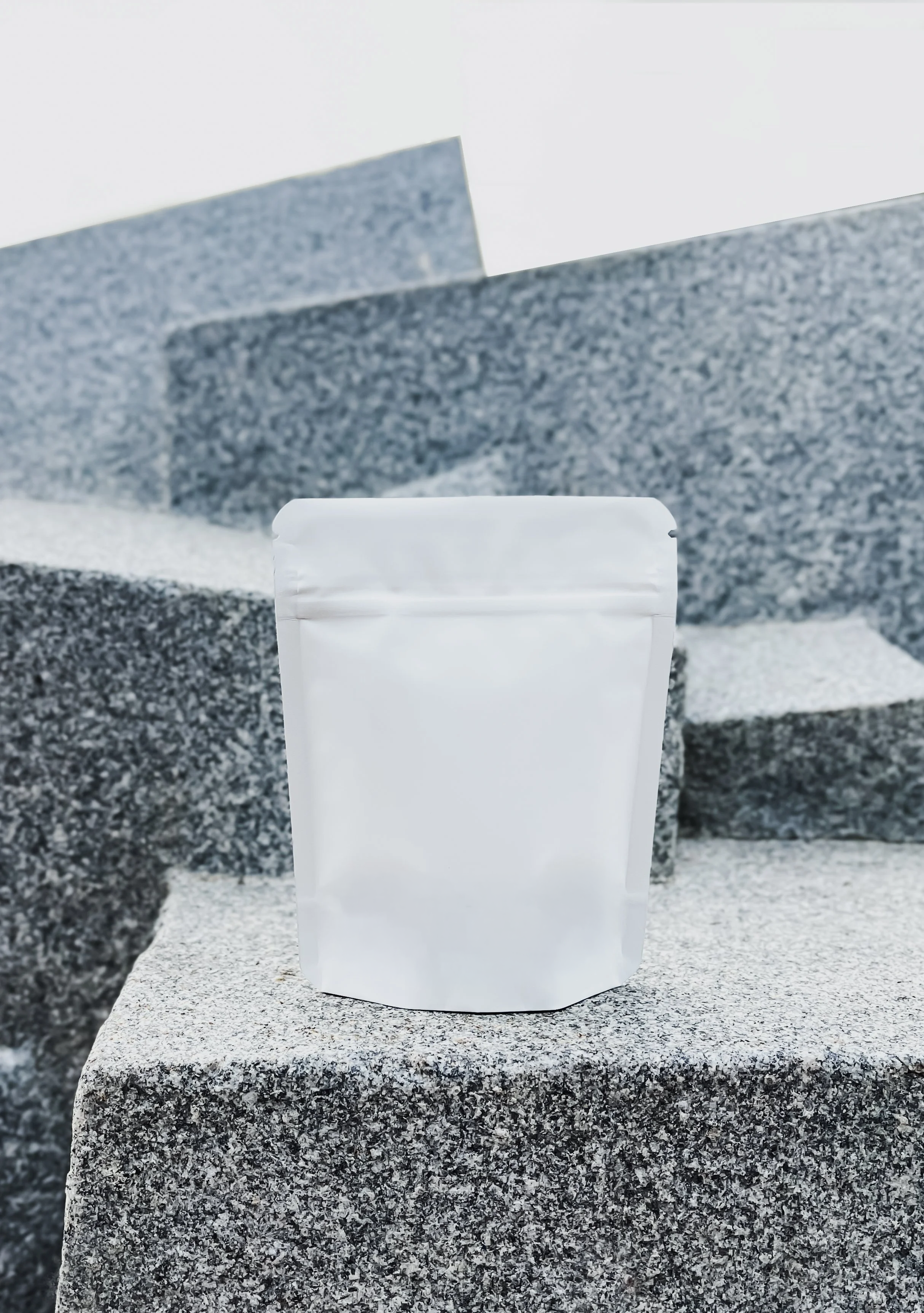 A white, resealable pouch standing on a stone surface with gray granite steps and background.