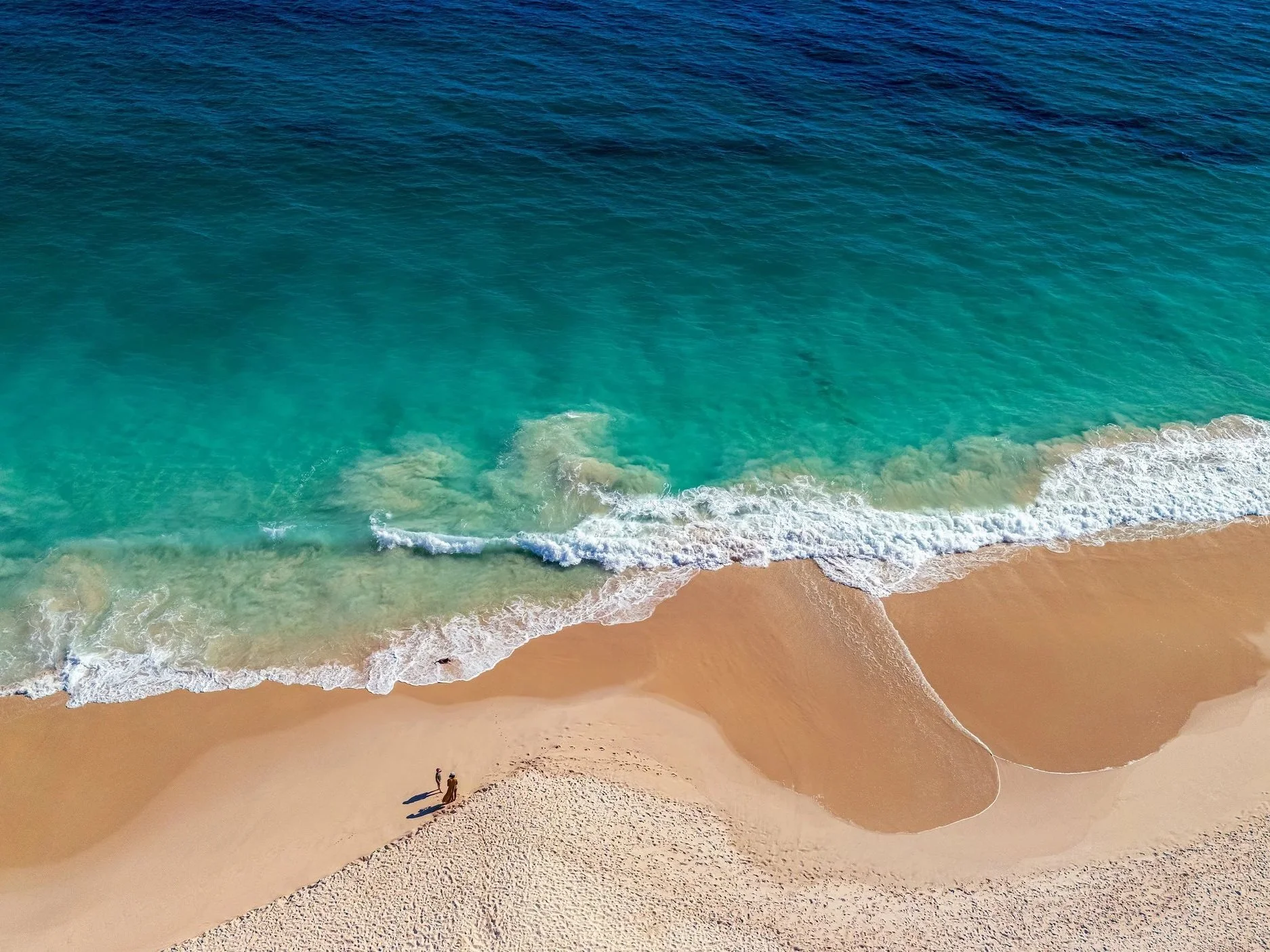 an aerial scene above a beach with two people talking a stroll