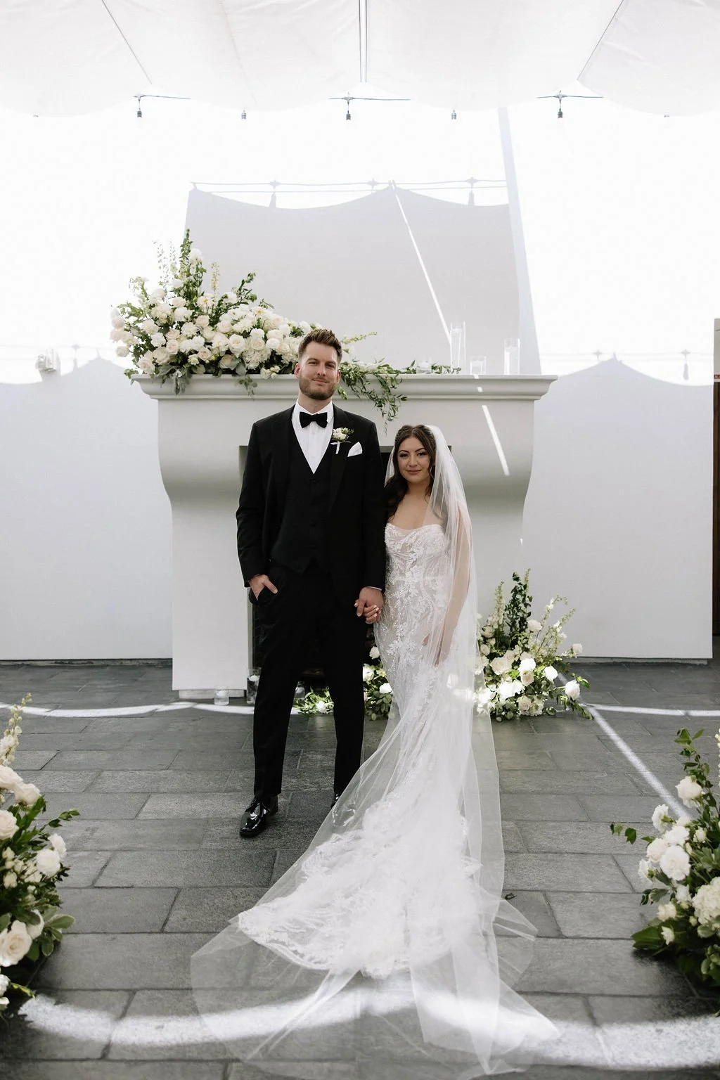 An elegant all-white palette transformed Blanco Urban Venue into a chic urban oasis for Bianca & John’s wedding. Lush roses, towering delphiniums, and touches of soft greenery lined the aisle, creating a bright, modern pathway toward the fireplace al