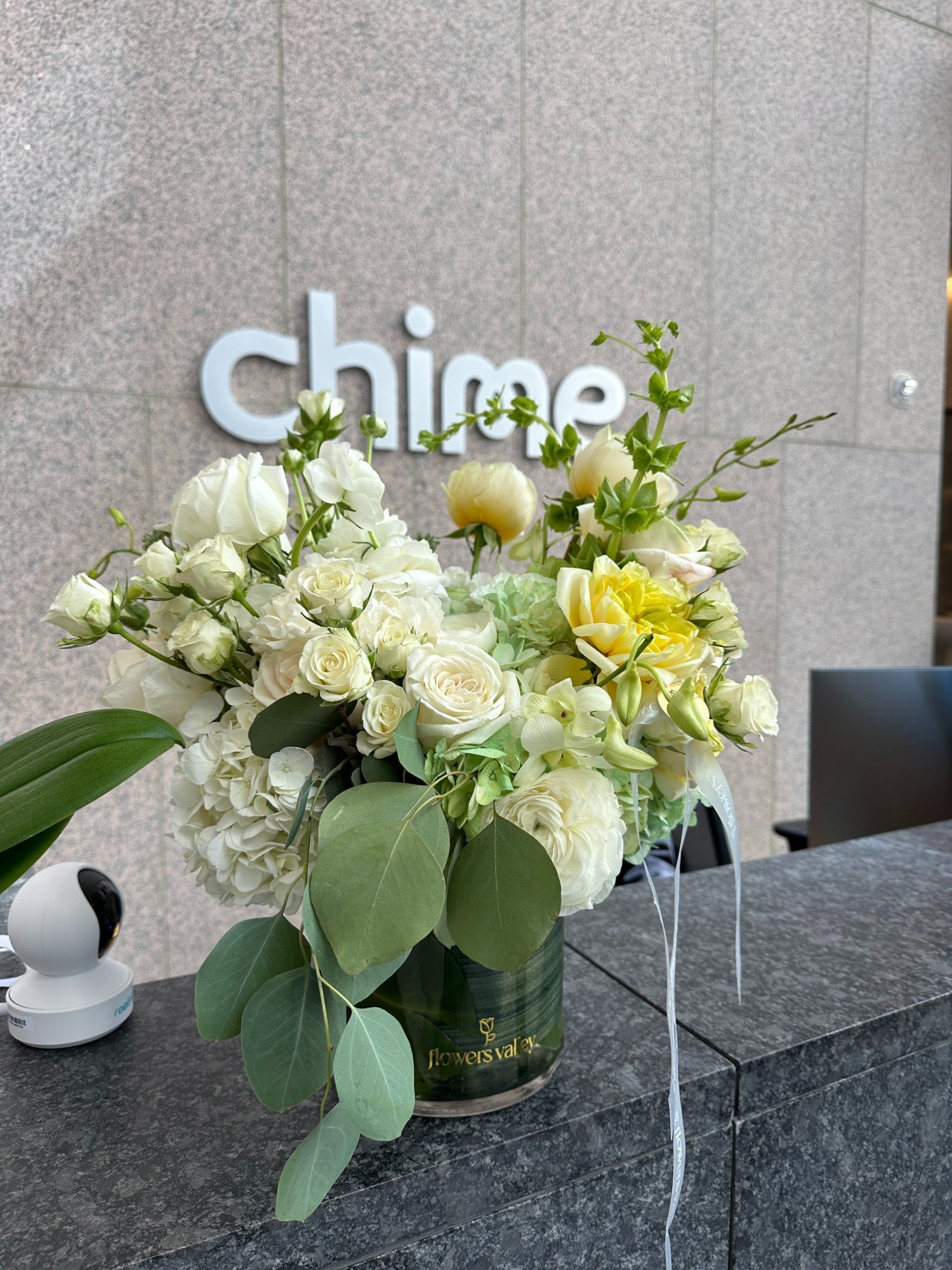 Festive floral arrangement featuring vibrant red poinsettias, candles, winter greenery, and seasonal accents, placed on a white pedestal with a natural outdoor background.