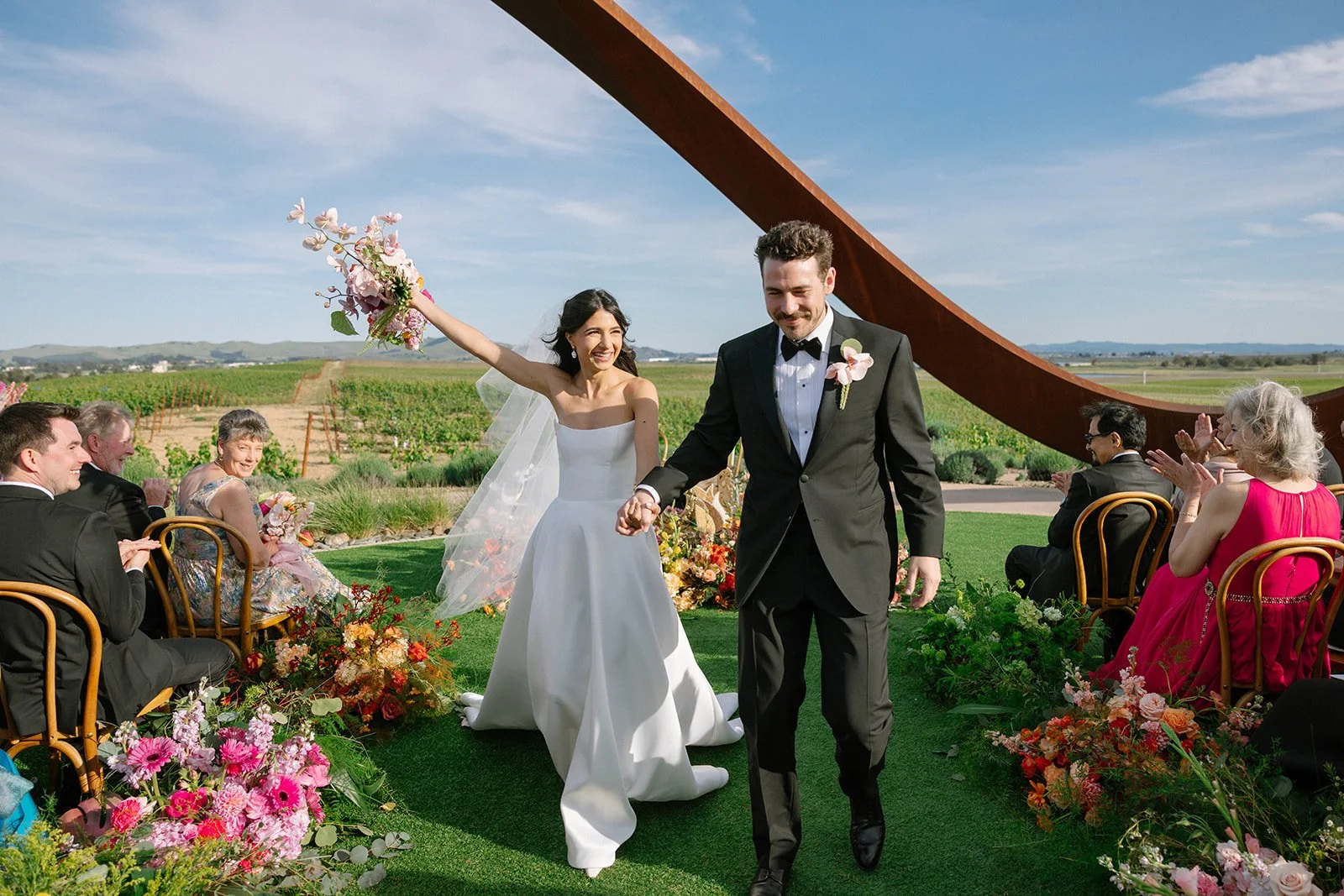 Vibrant Stanly Ranch wedding featuring bold orange, coral, fuchsia, and yellow wedding flowers. Explore lush bridal bouquets, ceremony floral installations, elevated aisle arrangements, and colorful reception centerpieces designed with premium blooms