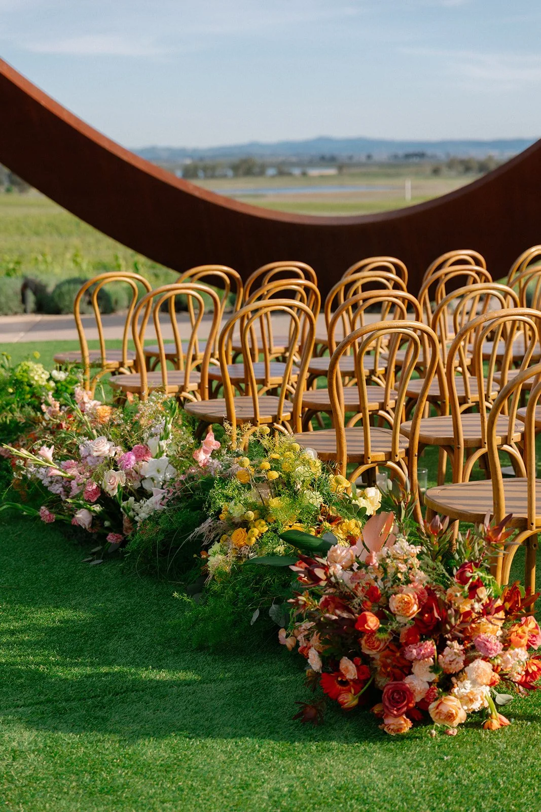 Vibrant Stanly Ranch wedding featuring bold orange, coral, fuchsia, and yellow wedding flowers. Explore lush bridal bouquets, ceremony floral installations, elevated aisle arrangements, and colorful reception centerpieces designed with premium blooms