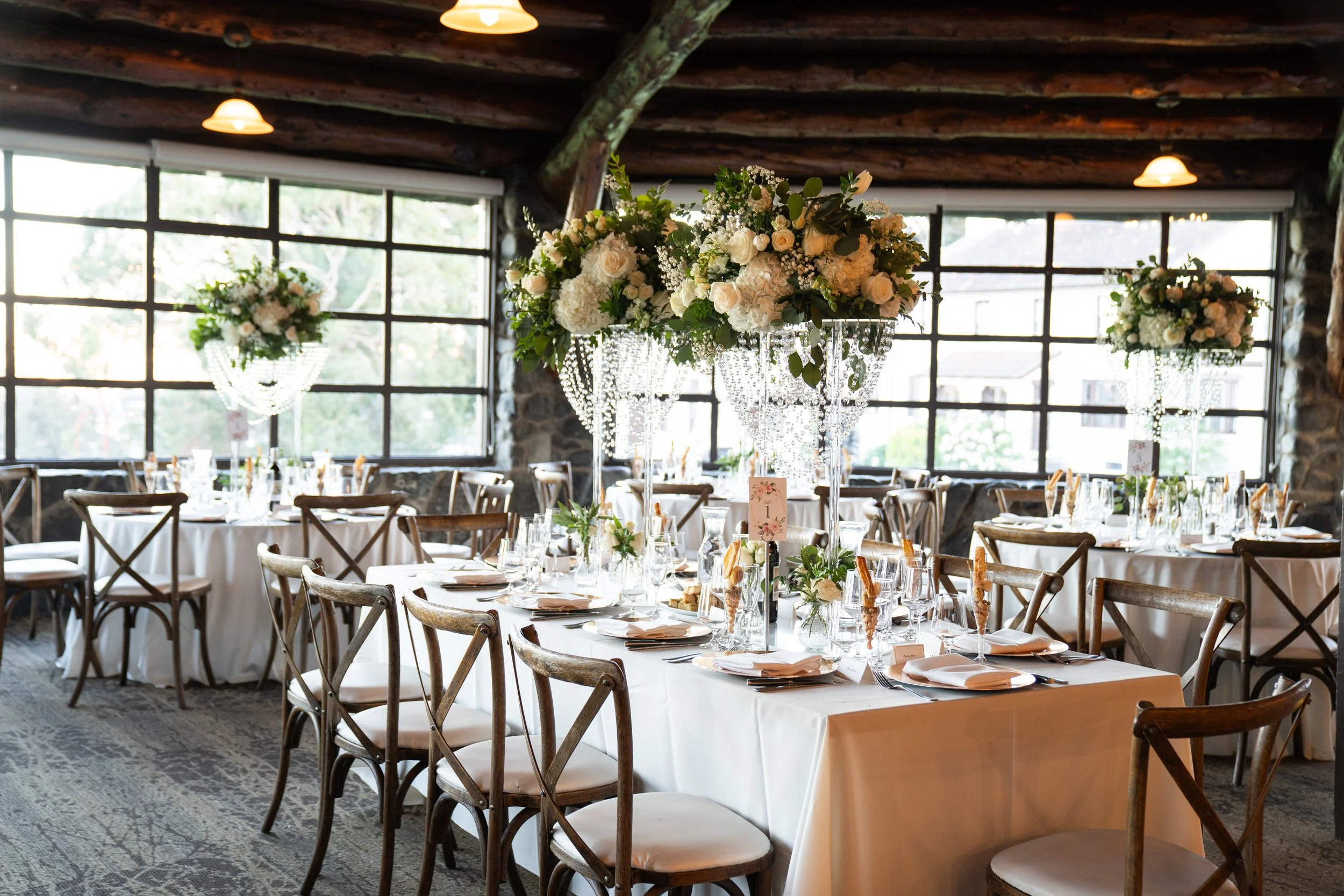 A rustic wedding reception with tables adorned with tall white and green floral centerpieces and crystal accents.