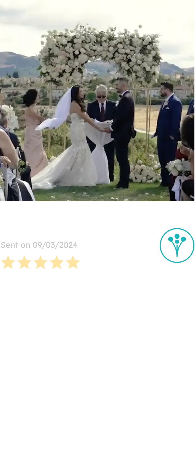 A couple stands hand-in-hand under a lush white floral arch during their outdoor wedding ceremony, with elegant bouquets designed by a San Francisco-based florist.