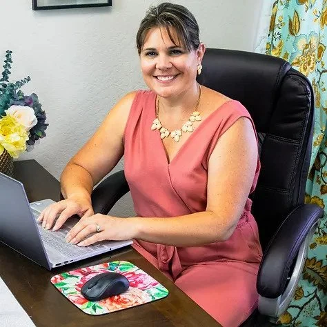 A professional wedding planner, one of our valued partners of The Flowers Valley, smiling confidently while working at her desk with floral accents in the background.
