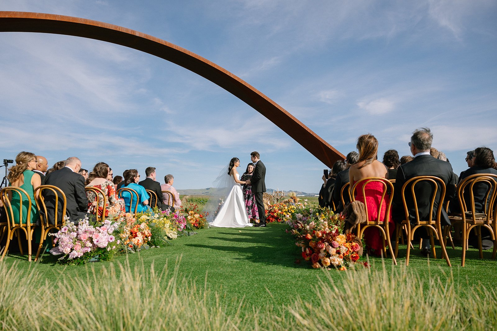Vibrant Stanly Ranch wedding featuring bold orange, coral, fuchsia, and yellow wedding flowers. Explore lush bridal bouquets, ceremony floral installations, elevated aisle arrangements, and colorful reception centerpieces designed with premium blooms