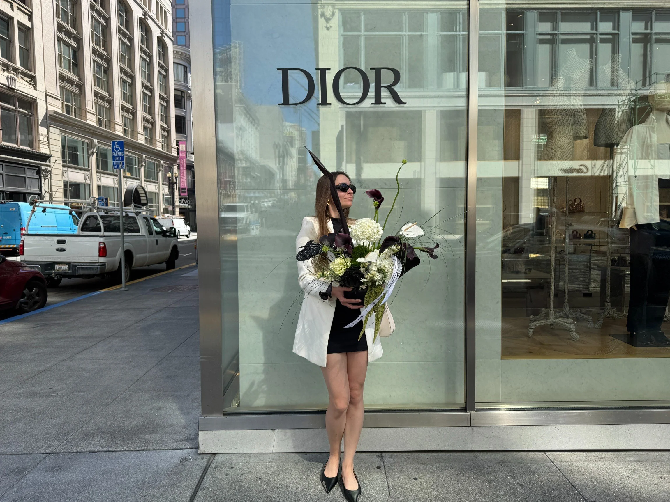 Elegant centerpiece featuring white anemones and lush greenery in a modern square vase, placed on a table with a soft purple glow, set at a corporate event.