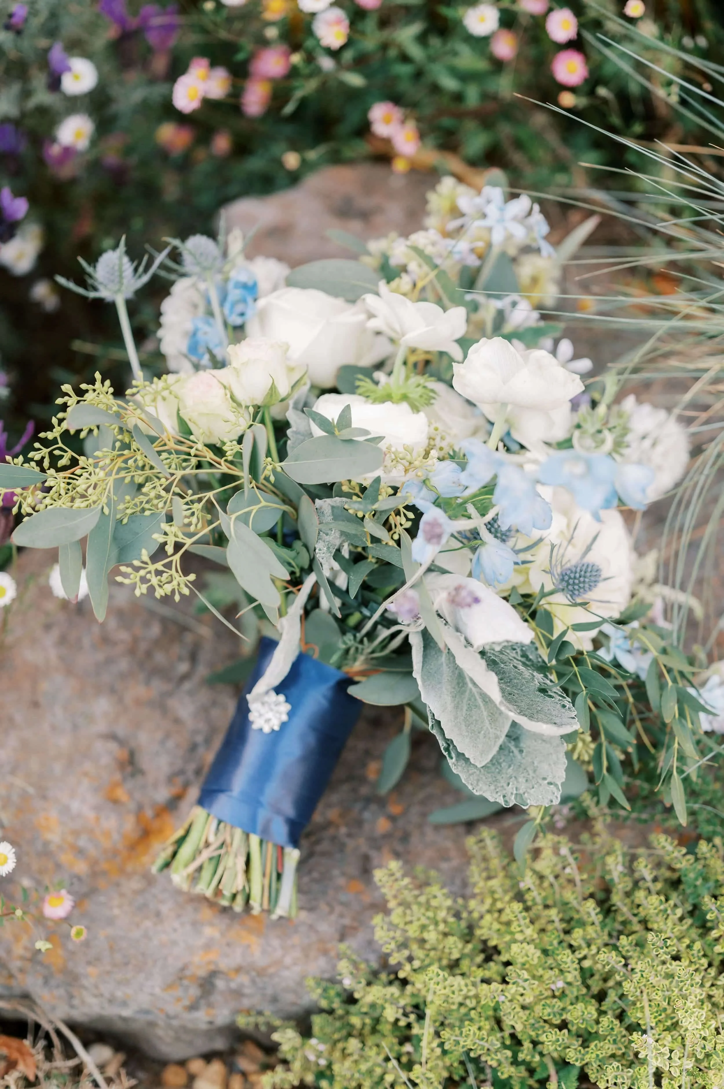 Close-up of a bridal bouquet featuring white roses, blue delphiniums, thistles, and eucalyptus.