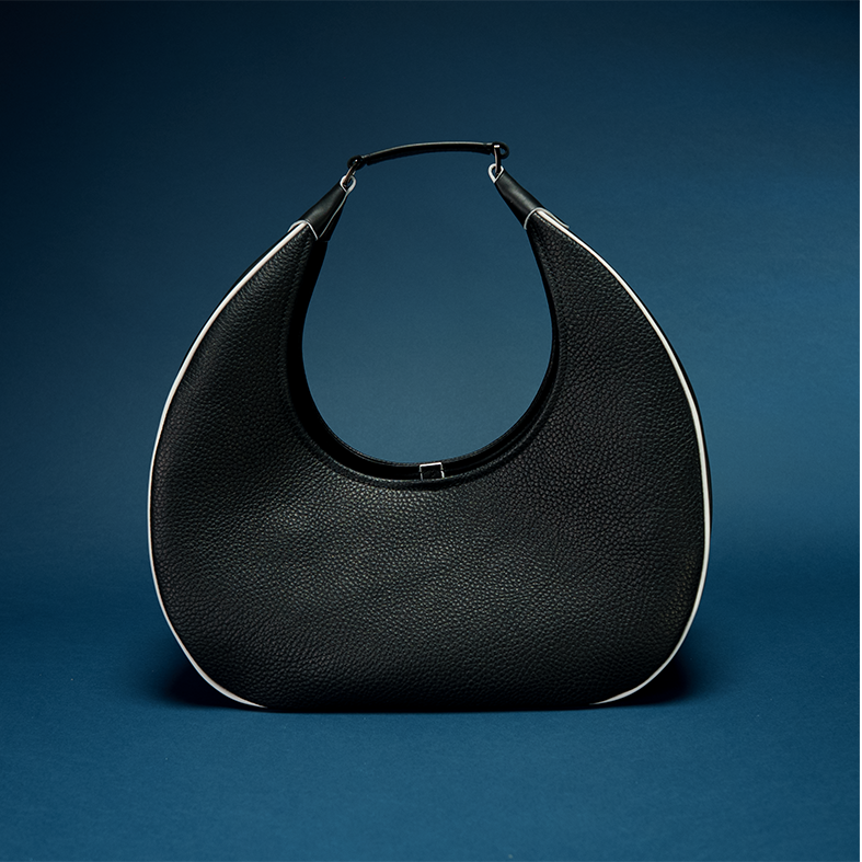 REINA Shoulder Bag in Midnight — pebbled black calf leather crescent silhouette with white piping trim and gunmetal hardware, paired with the RINA La Bori sneaker