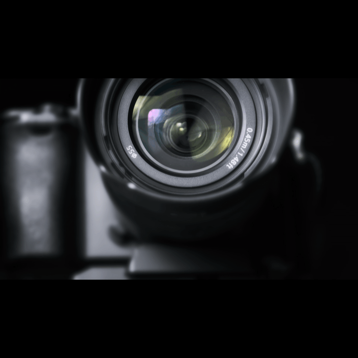 Close-up of a DSLR camera lens, focusing on the front element, with a dark background.