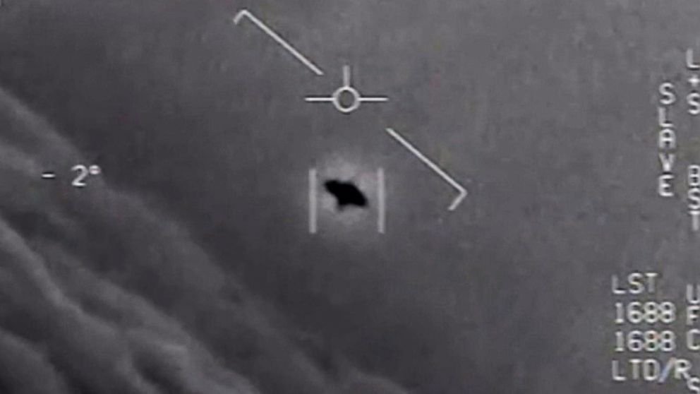 Grainy black-and-white infrared thermal imagery from a U.S. Navy F/A-18 targeting pod, showing an elongated white oblong object centered in the crosshairs against a dark sky, with radar and heading data visible in the heads-up display.