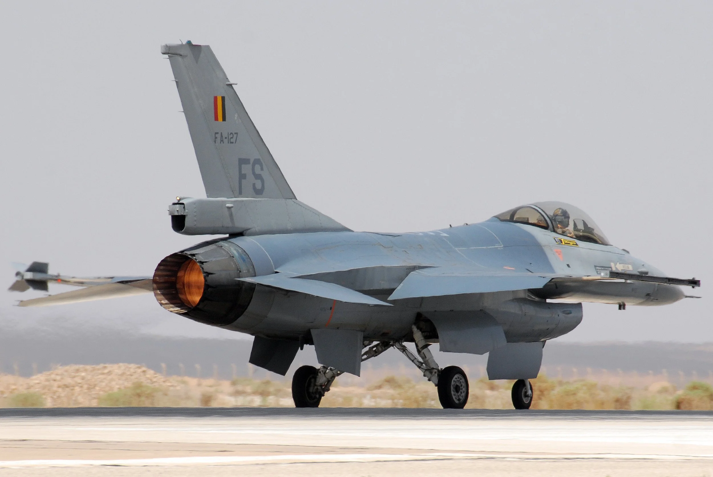 A Belgian Air Force F-16 Fighting Falcon fighter jet on a runway preparing for takeoff, with ground crew visible.