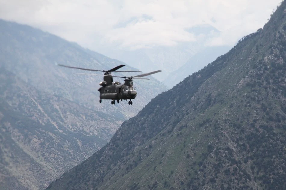 A U.S. Army CH-47 Chinook, a large twin-rotor military helicopter, in flight against a mountainous backdrop.