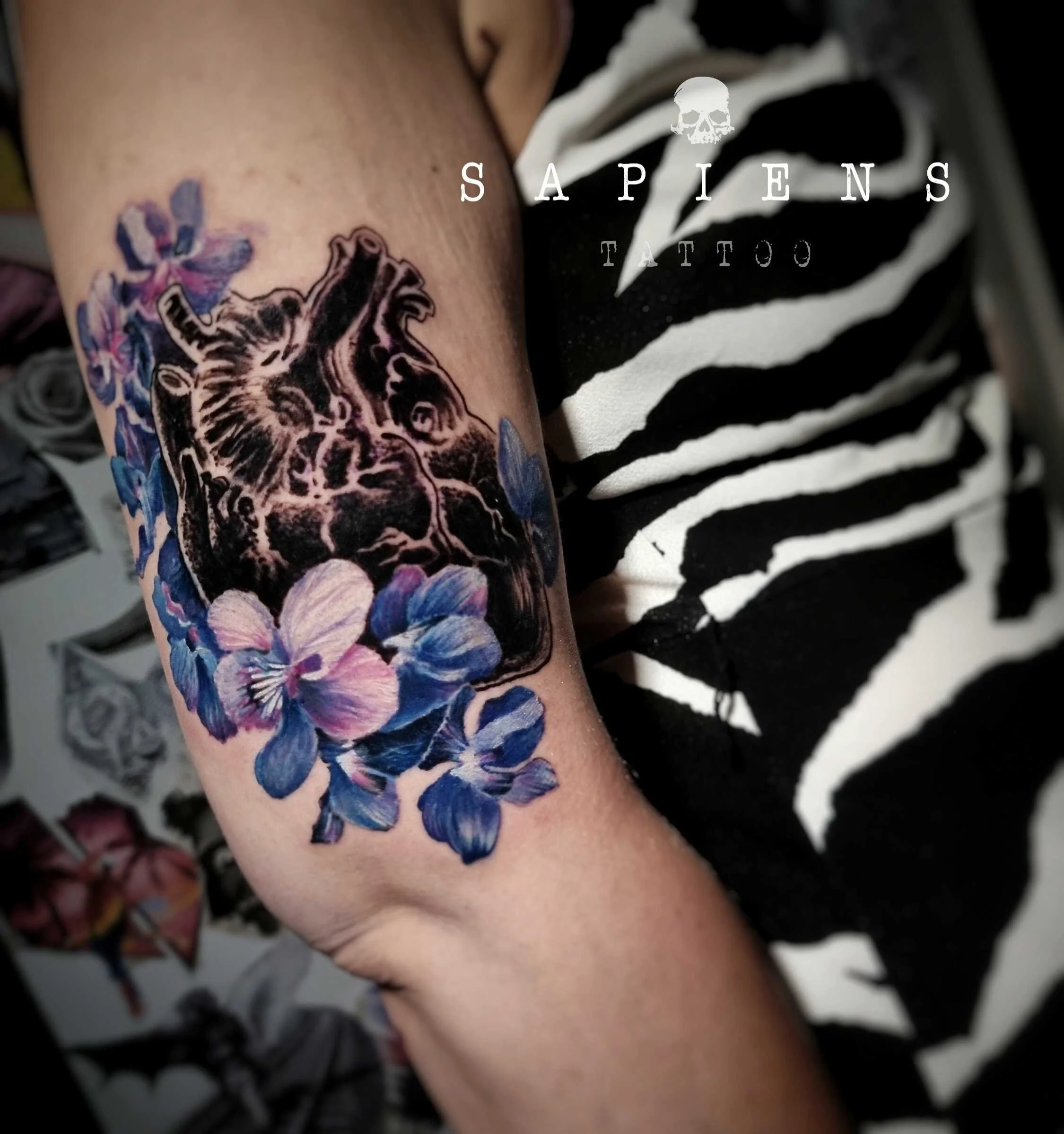 tatuaj pe brat cu o inima albastra si flori albastre si violet in stil realistic