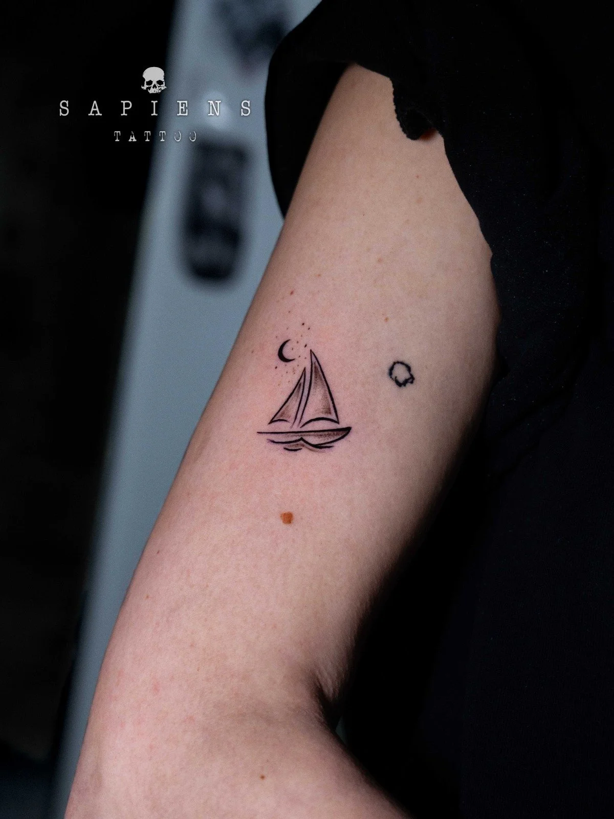 tatuaj extrem de mic realizat din linii fine cu o barcuta si o semiluna inconjurata de stele