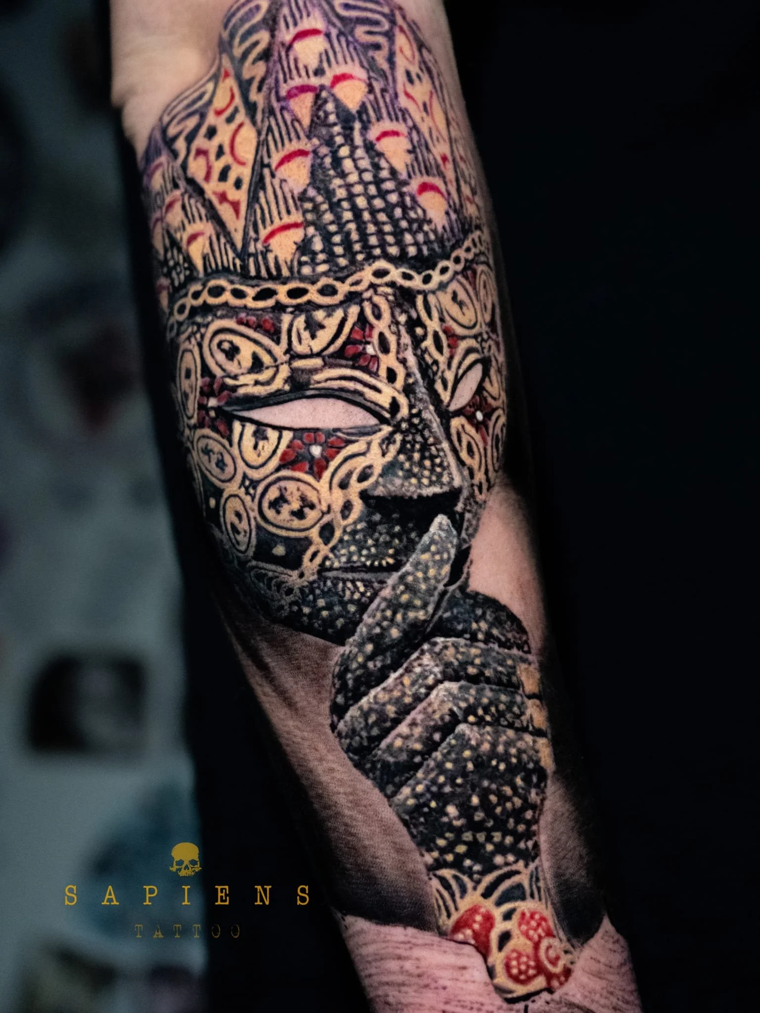 tatuaj pe antebrat cu o masca si cu tus rosu