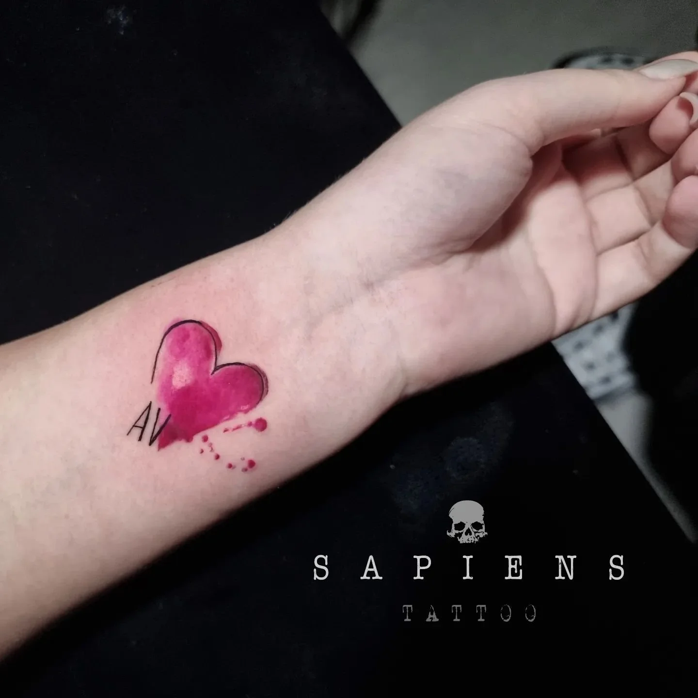 tatuaj mic pe incheietura mainii cu o inima roz si splashuri de culoare roz si doua initiale