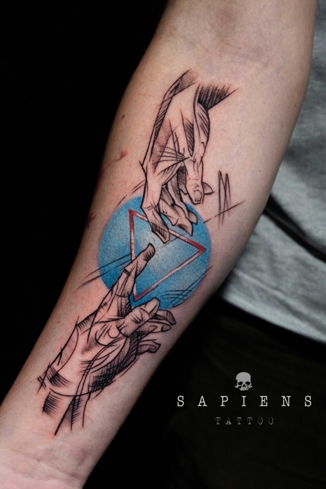 tatuaj pe antebratul unui barbat cu referinta mainile lui adam realizat in stil sketch si fundal cu tus albastru