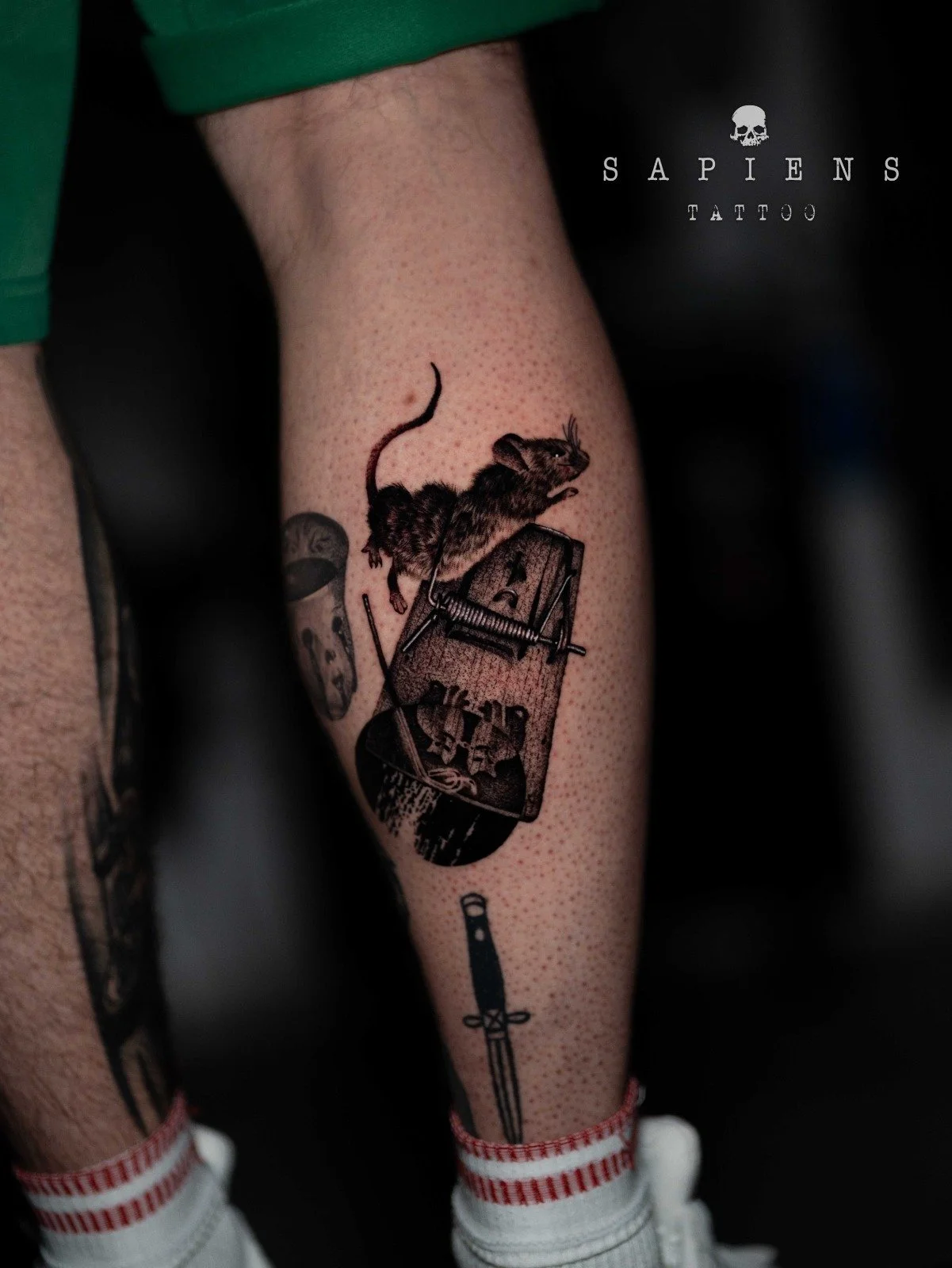 tatuaj in stil dark realizat pe pulpa piciorului spate cu un soarece prins in capcana si alte elemete dark in jurul sau