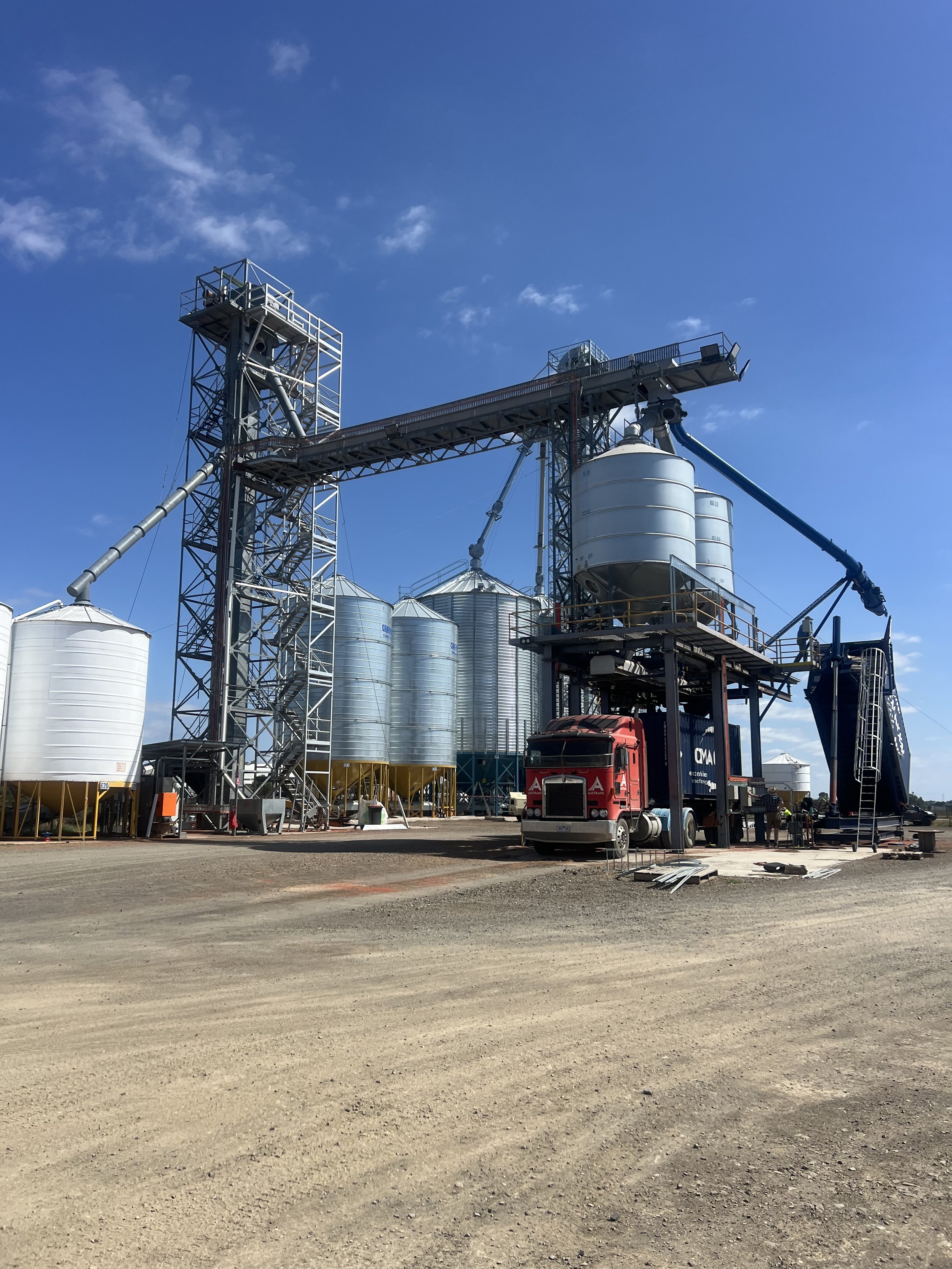 Industrial farm with silos, a truck, and construction equipment under a blue sky.