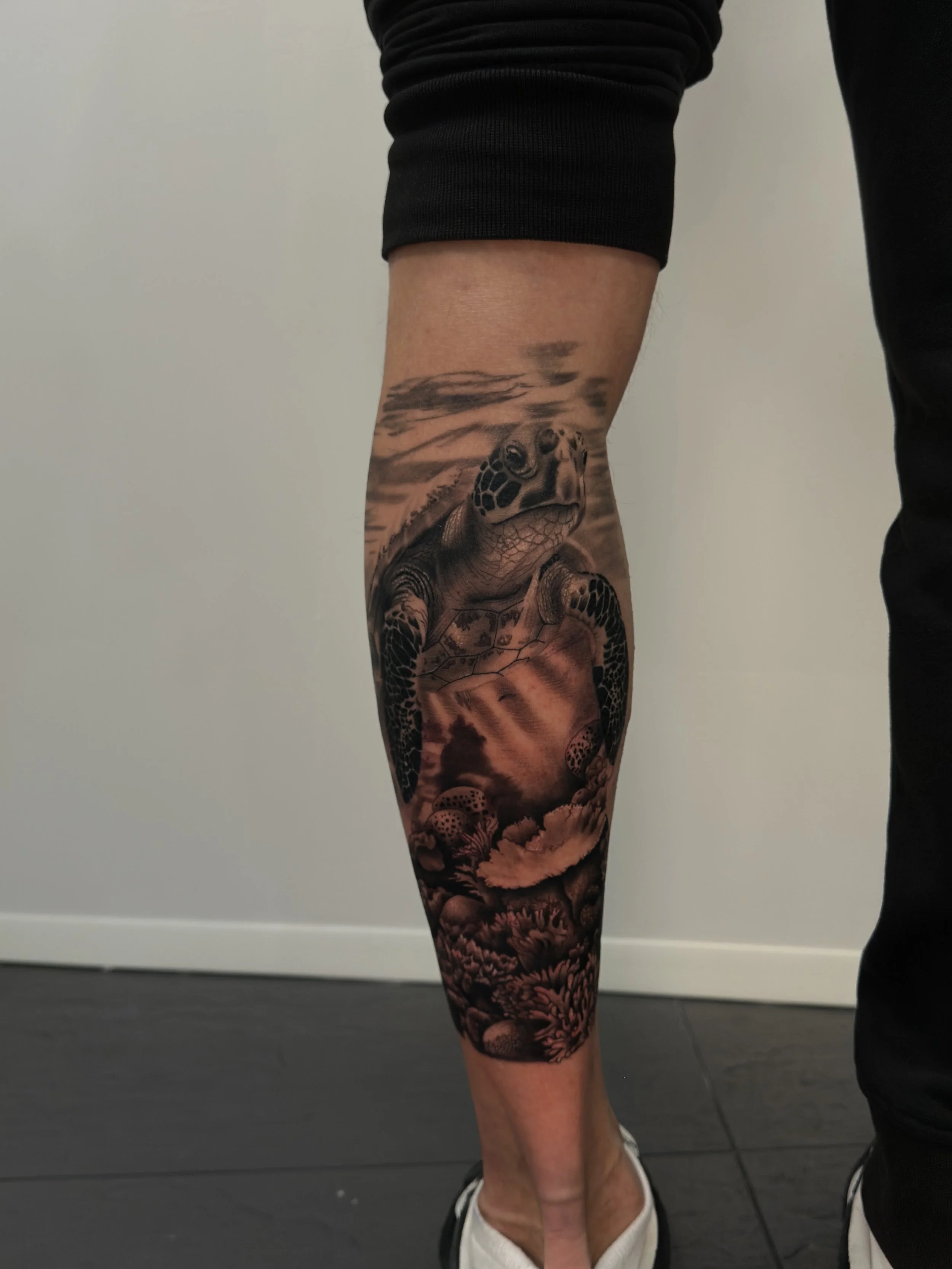Tattoo eines Meeresschildkröte mit Unterwasserlandschaft auf dem Bein einer Person.