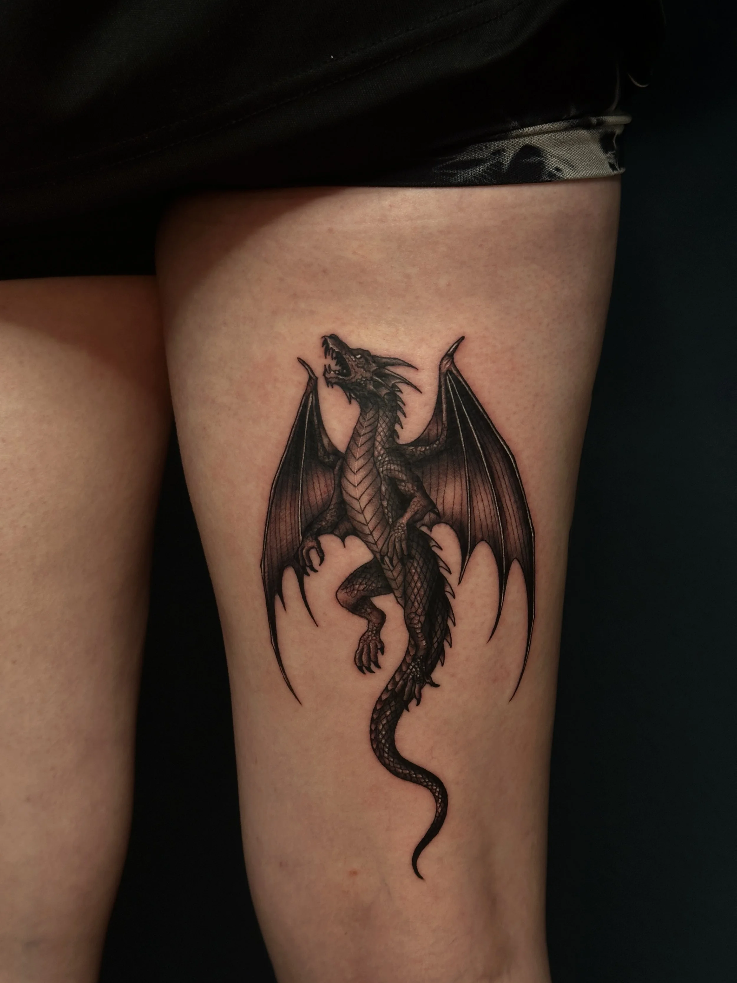 Tattoo eines schwarzen Drachen auf dem Oberschenkel.