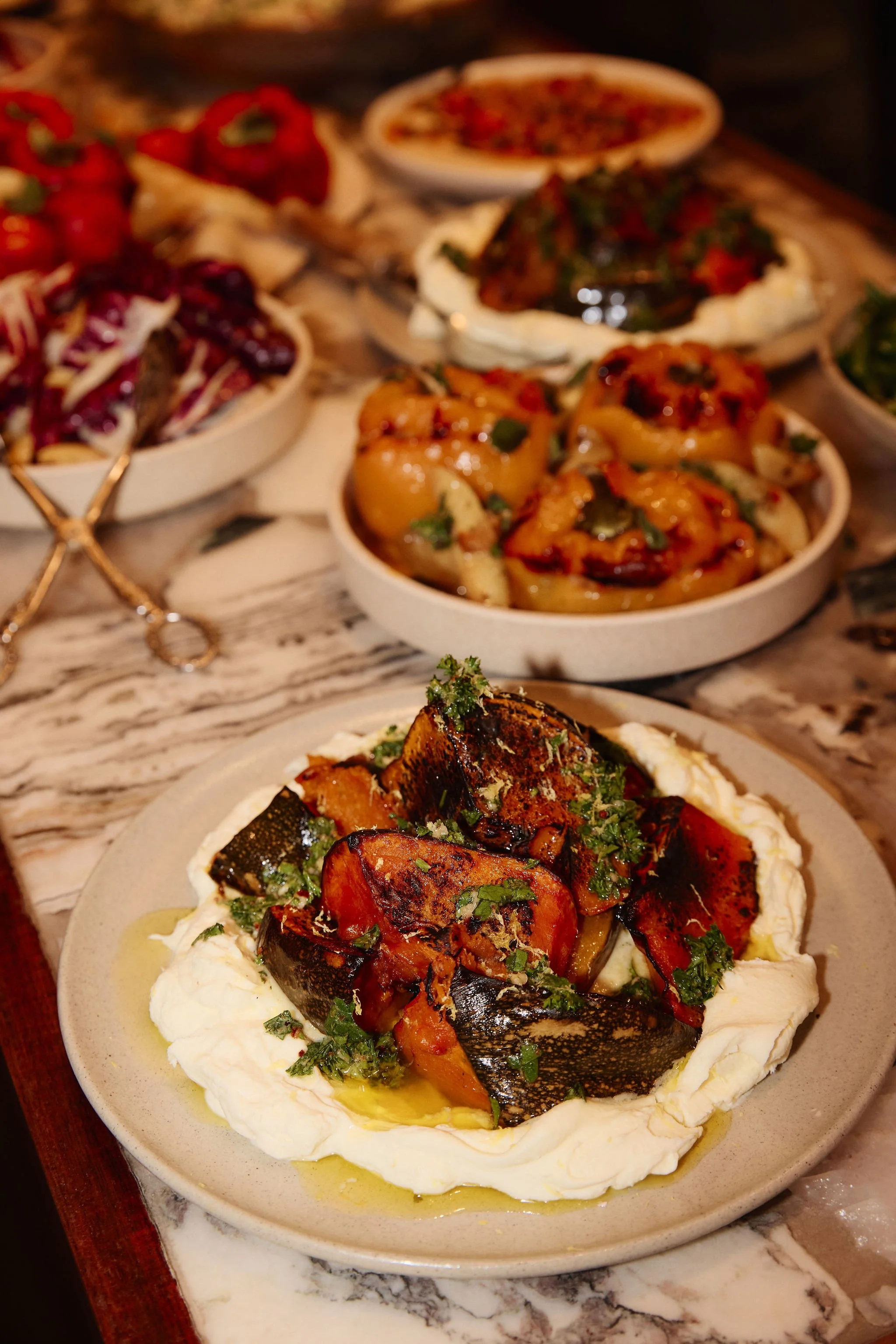 A plate of roasted vegetables on a bed of creamy spread garnished with herbs, drizzled with olive oil, served on a marble surface.