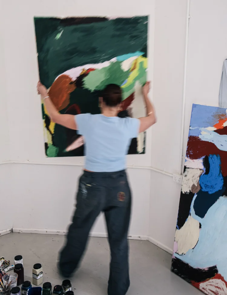 An artist hanging a large painting in the studio