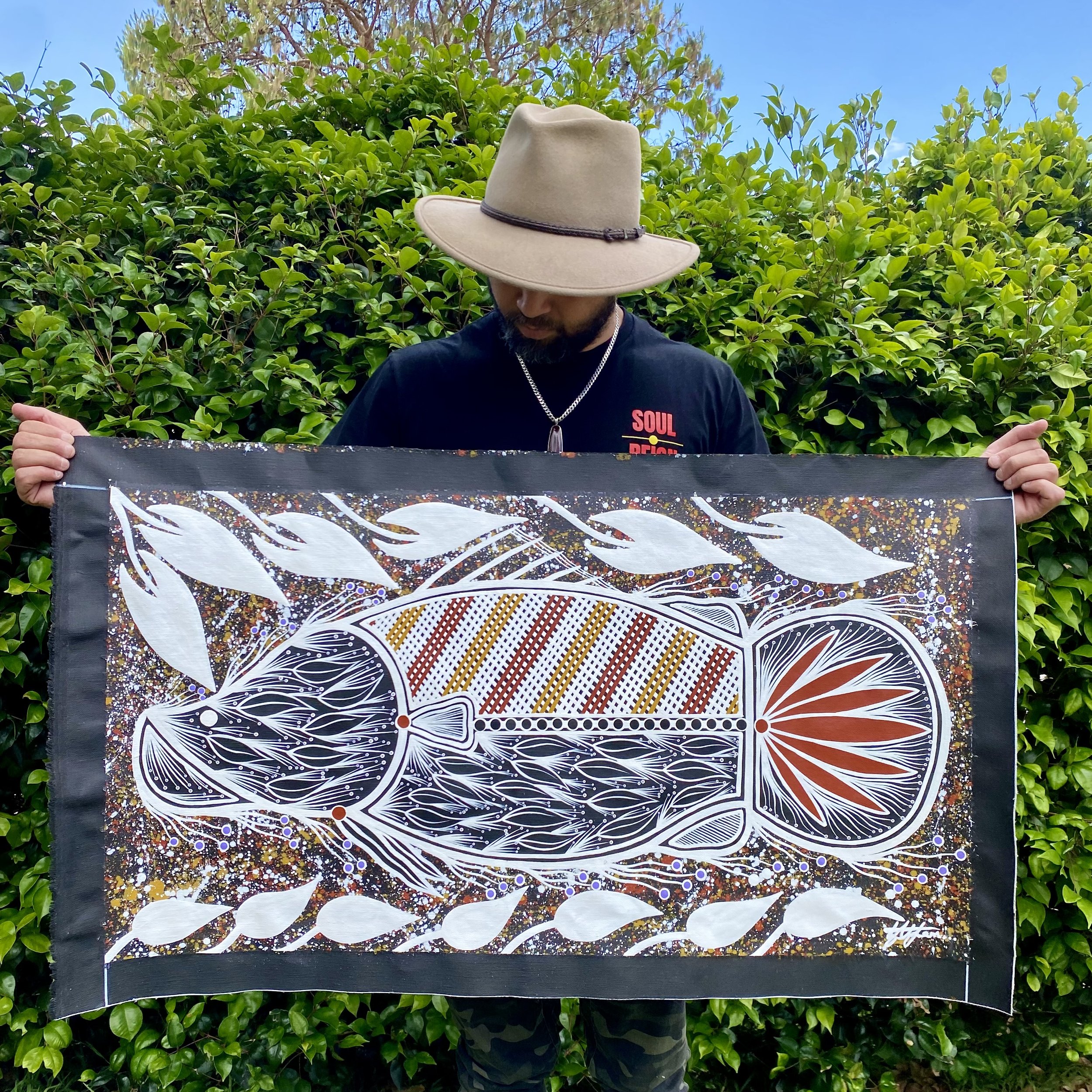 Painting of a barramundi swimming upstream with vibrant waterlilies, symbolising resilience, renewal, and cultural connection, created by artist Lyle Ah Sam