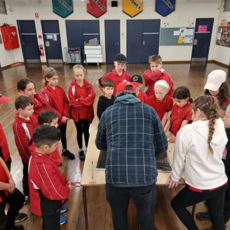 Students gathered around artist Lyle Ah Sam observing live Aboriginal artwork during school session