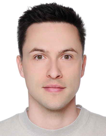 Nahaufnahme eines jungen Mannes mit dunklen Haaren und heller Haut, trägt ein graues Hemd, blickt direkt in die Kamera.